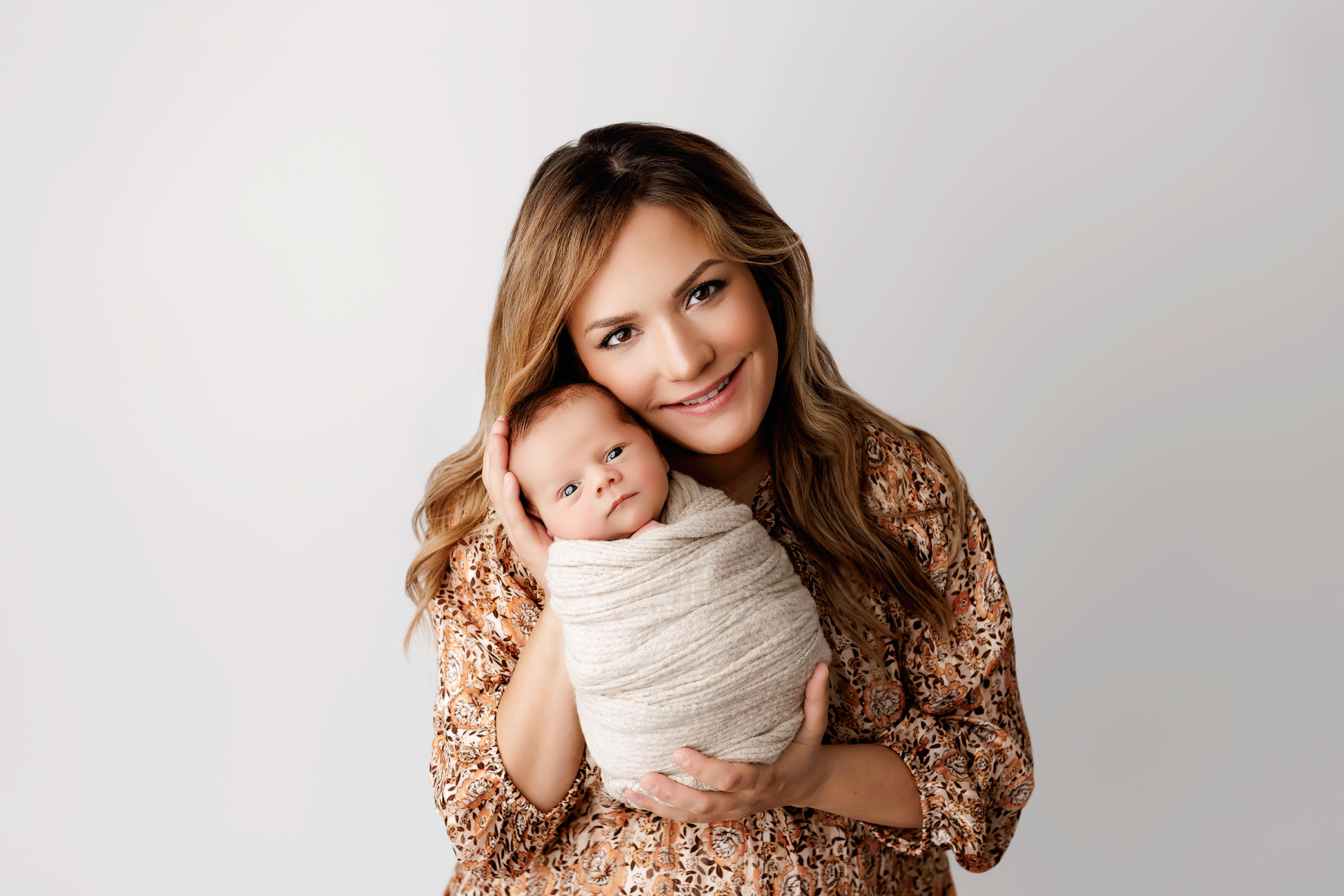 Mother holding her awake swaddled newborn baby during studio portrait session.