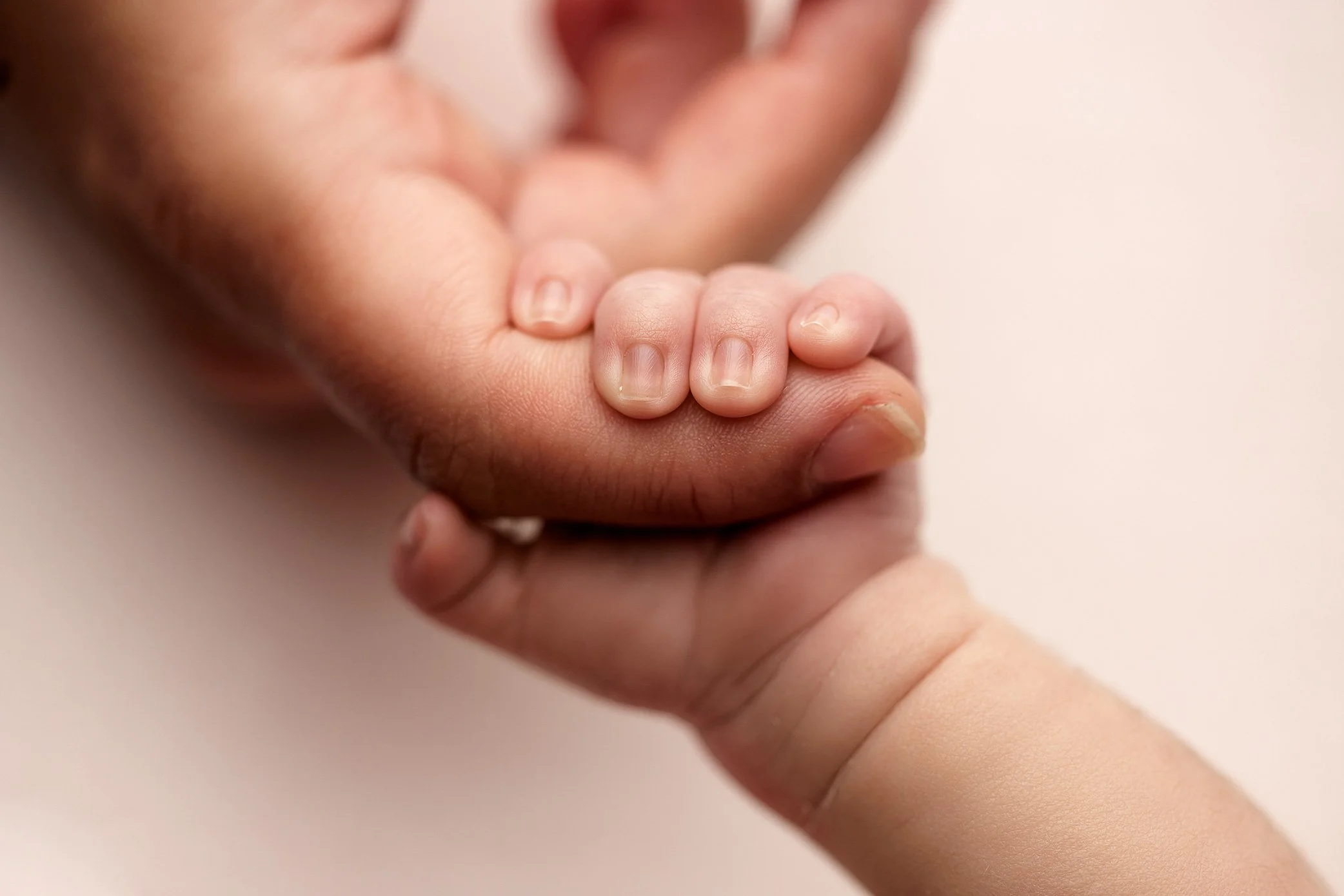 Close up of newborn baby’s tiny hand grasping mother's finger for size comparison.