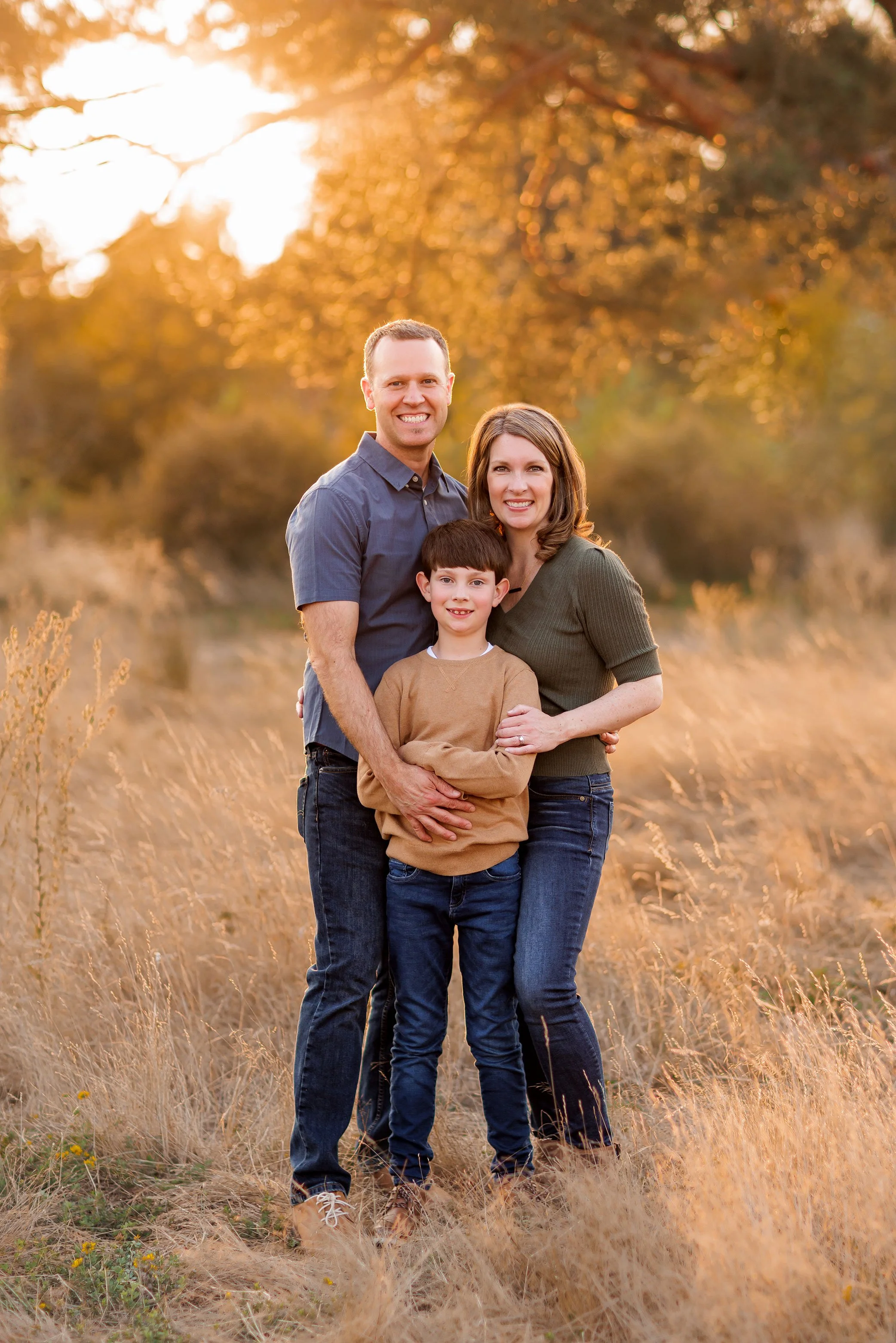 Family of three standing close together in golden field at sunset during Salem Oregon outdoor family photography session