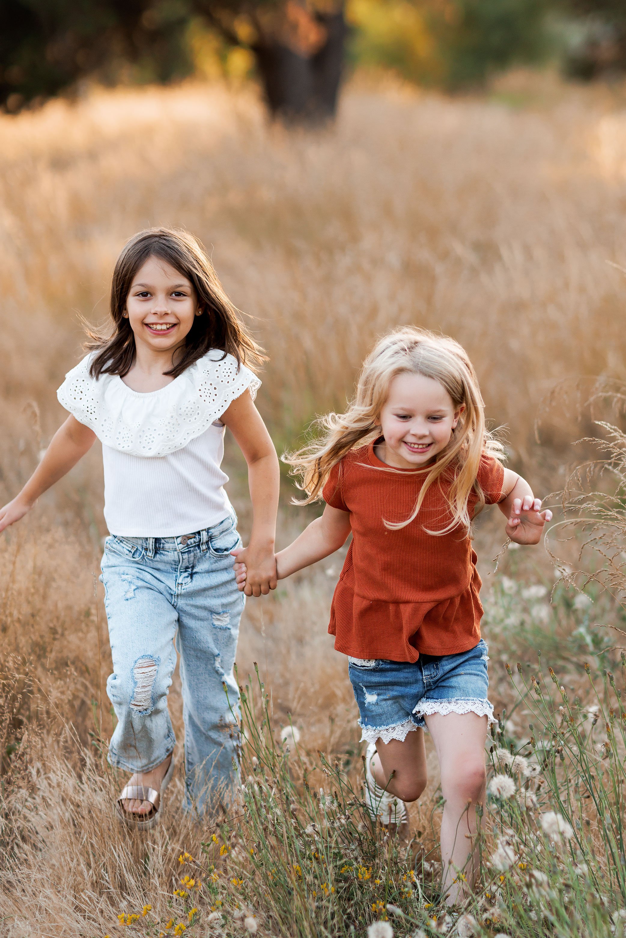 Two sisters holding hands and running through golden field during outdoor family photography session in Salem Oregon