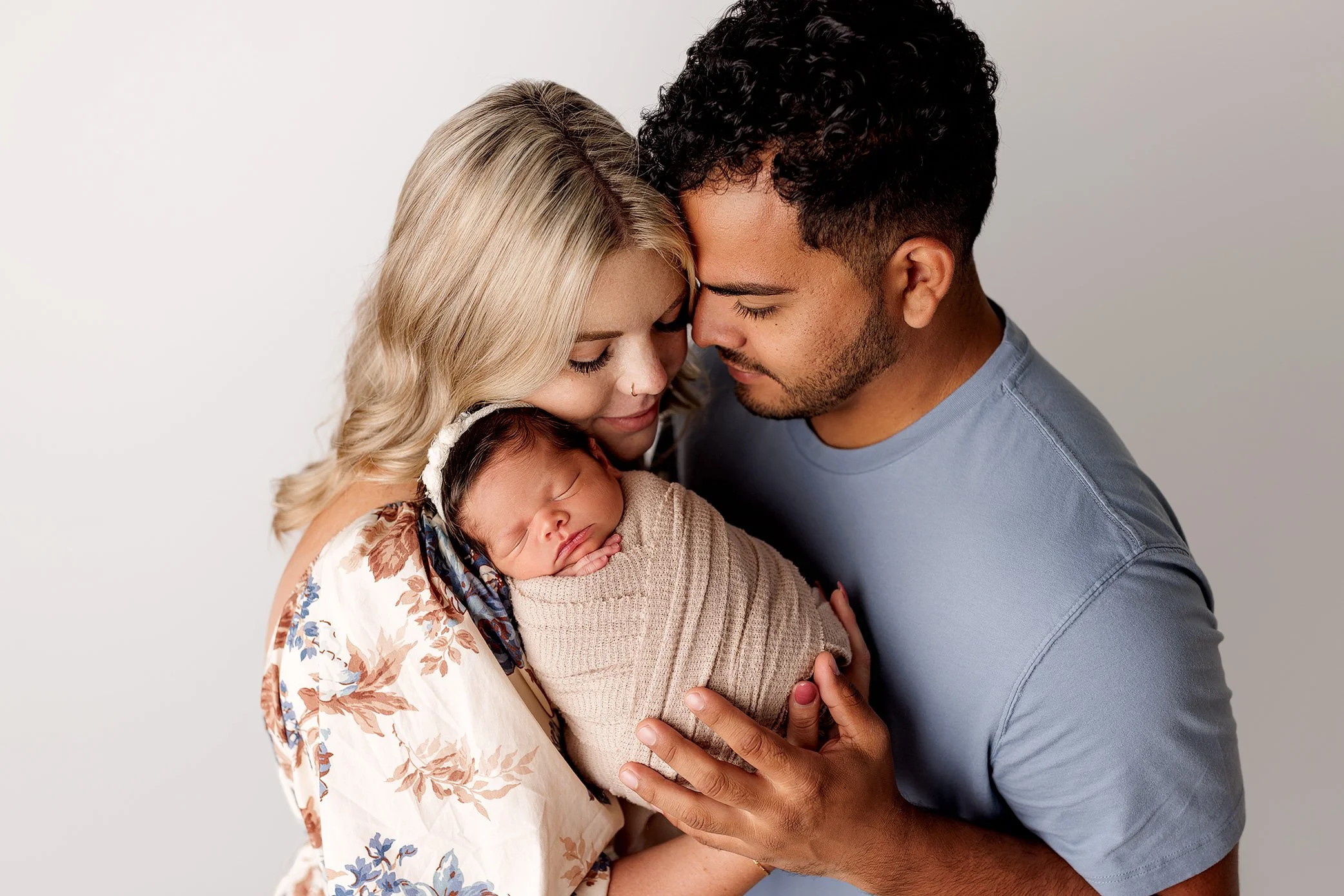 Mother and father gently holding their swaddled newborn baby during studio portrait session.