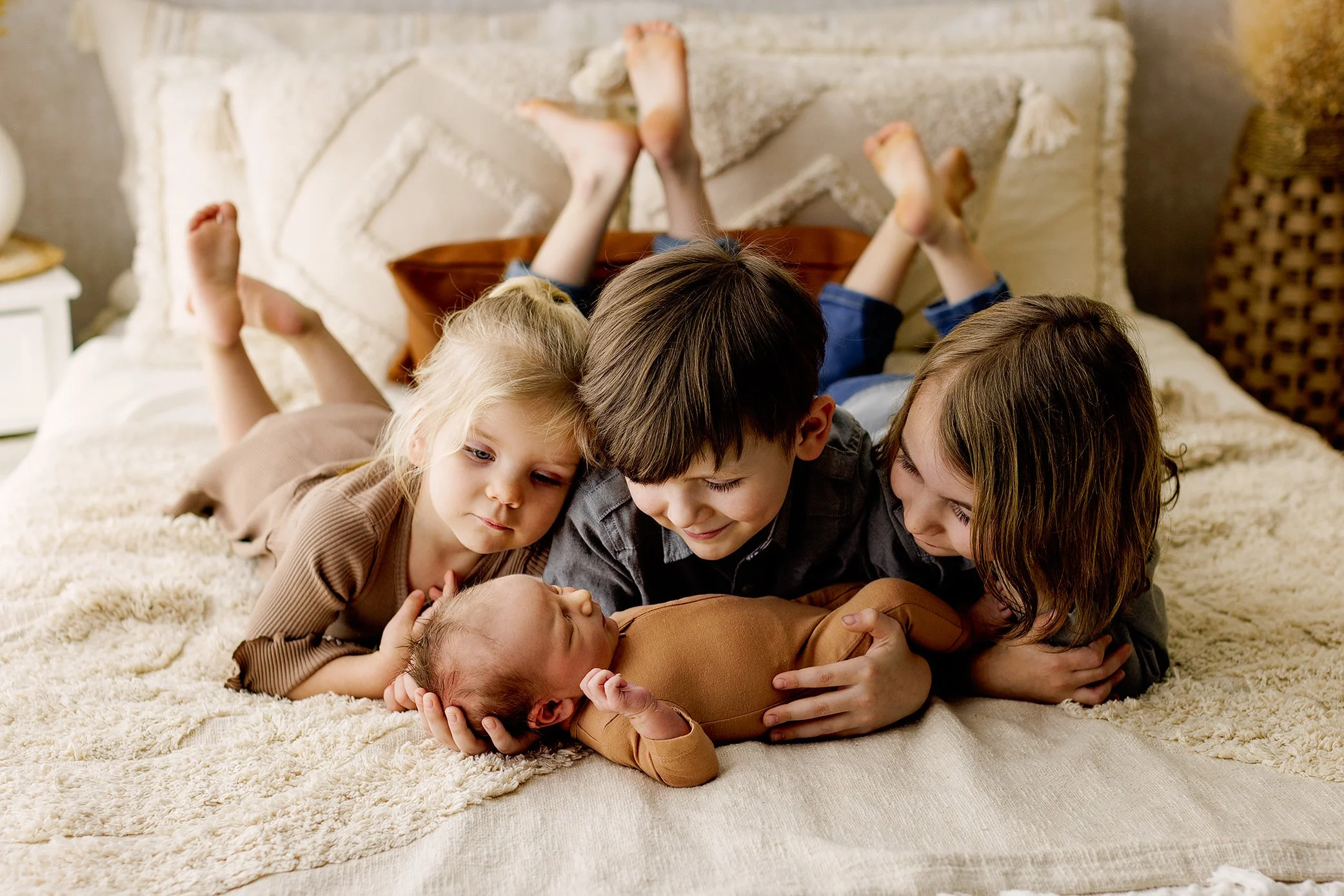 Three siblings laying together and admiring newborn baby during studio newborn session.