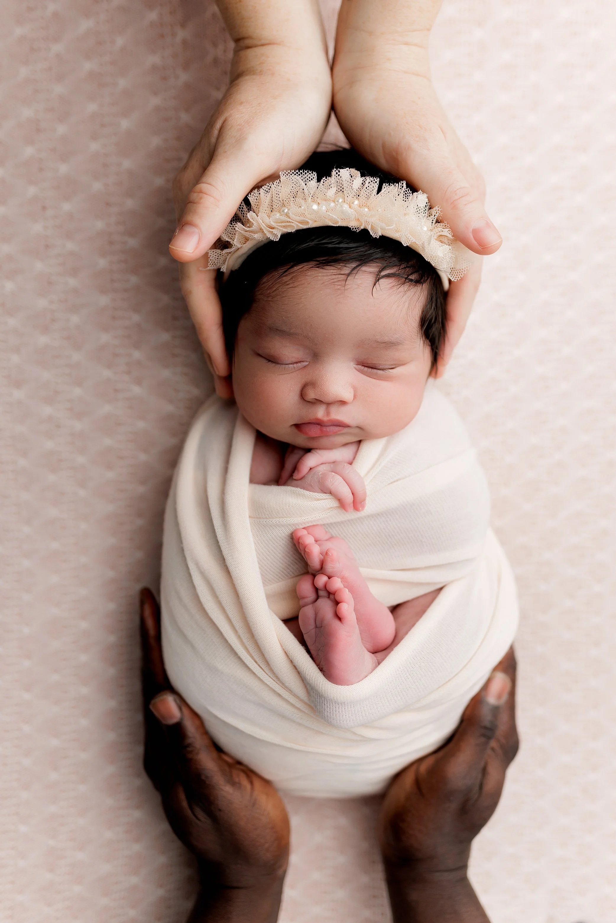 Newborn Girl snuggled safely with mom and dad's hands on her.