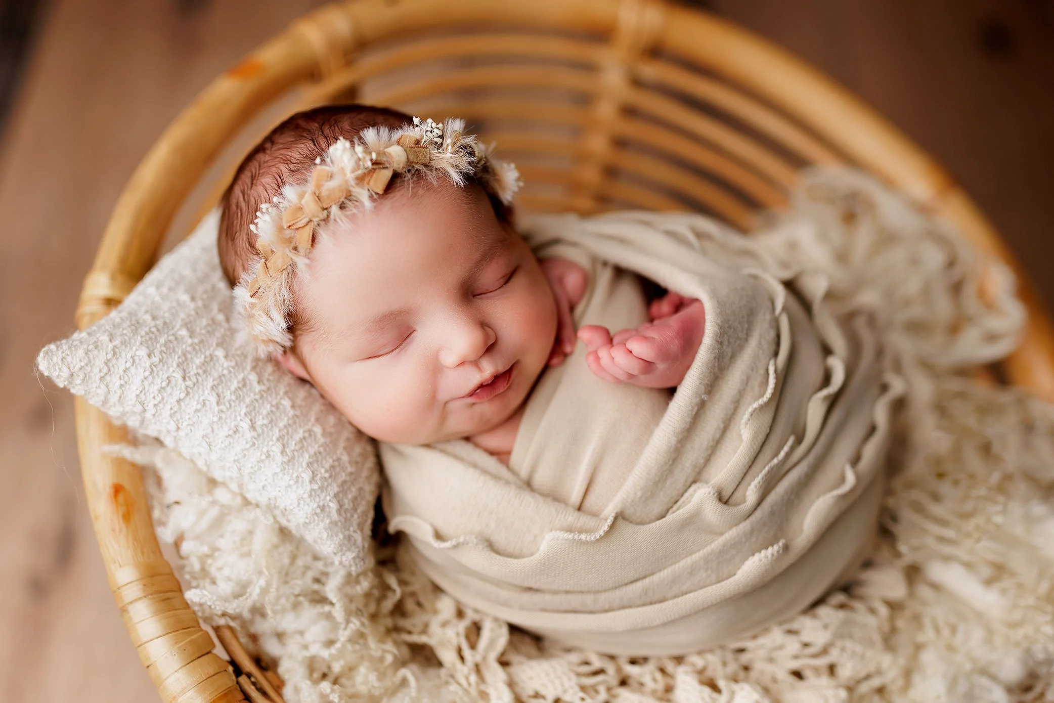 Sleeping newborn baby posed in a basket wearing a delicate neutral headband