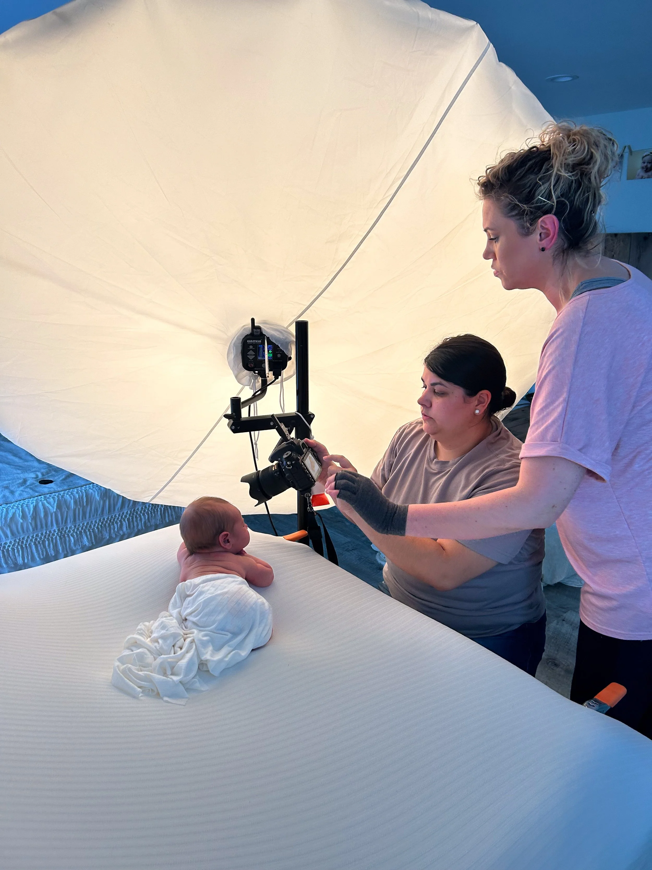 One-on-one newborn photography mentoring session with photographer reviewing camera settings while baby is safely posed on beanbag