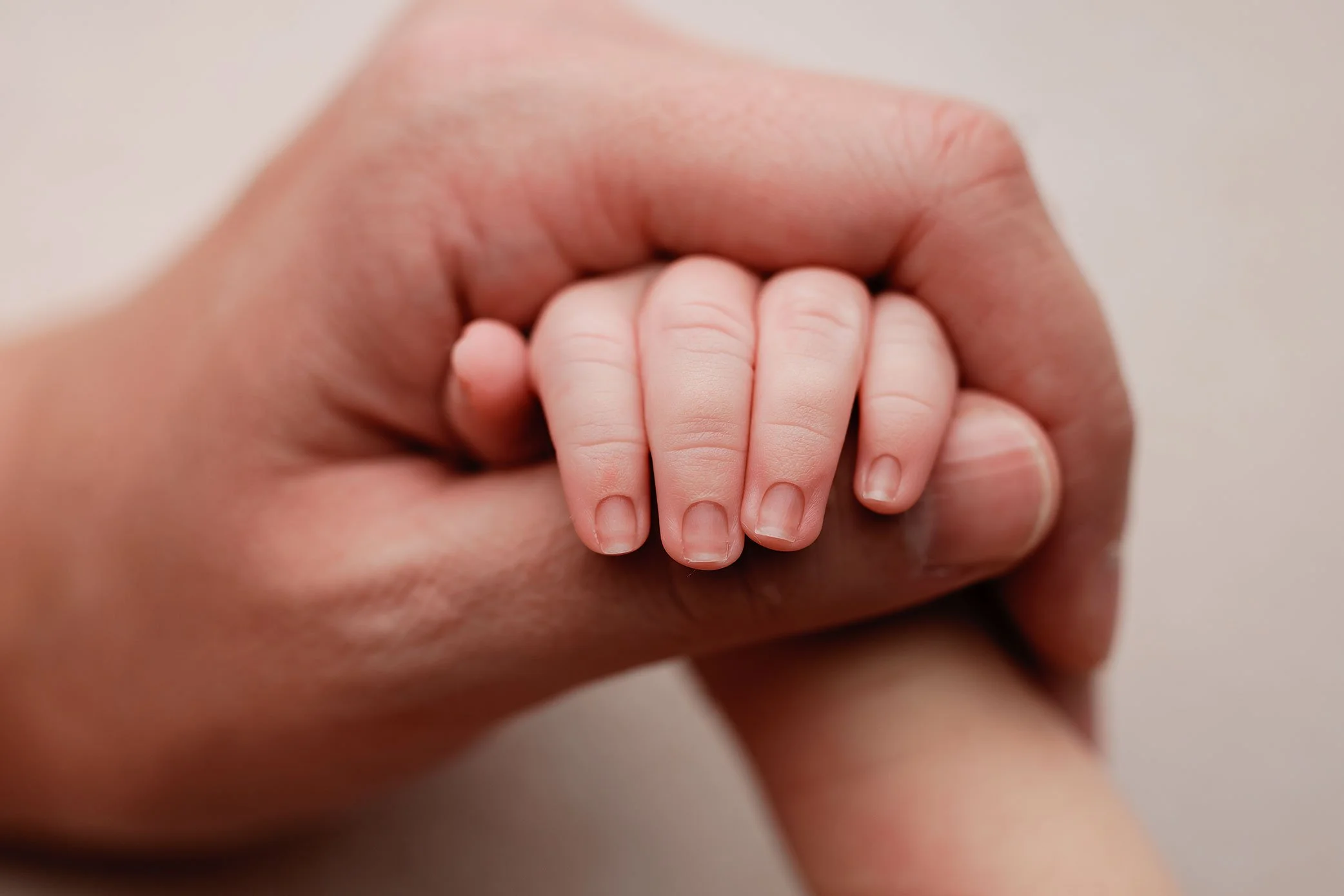 Close up of newborn baby’s tiny hand resting gently on father’s finger.