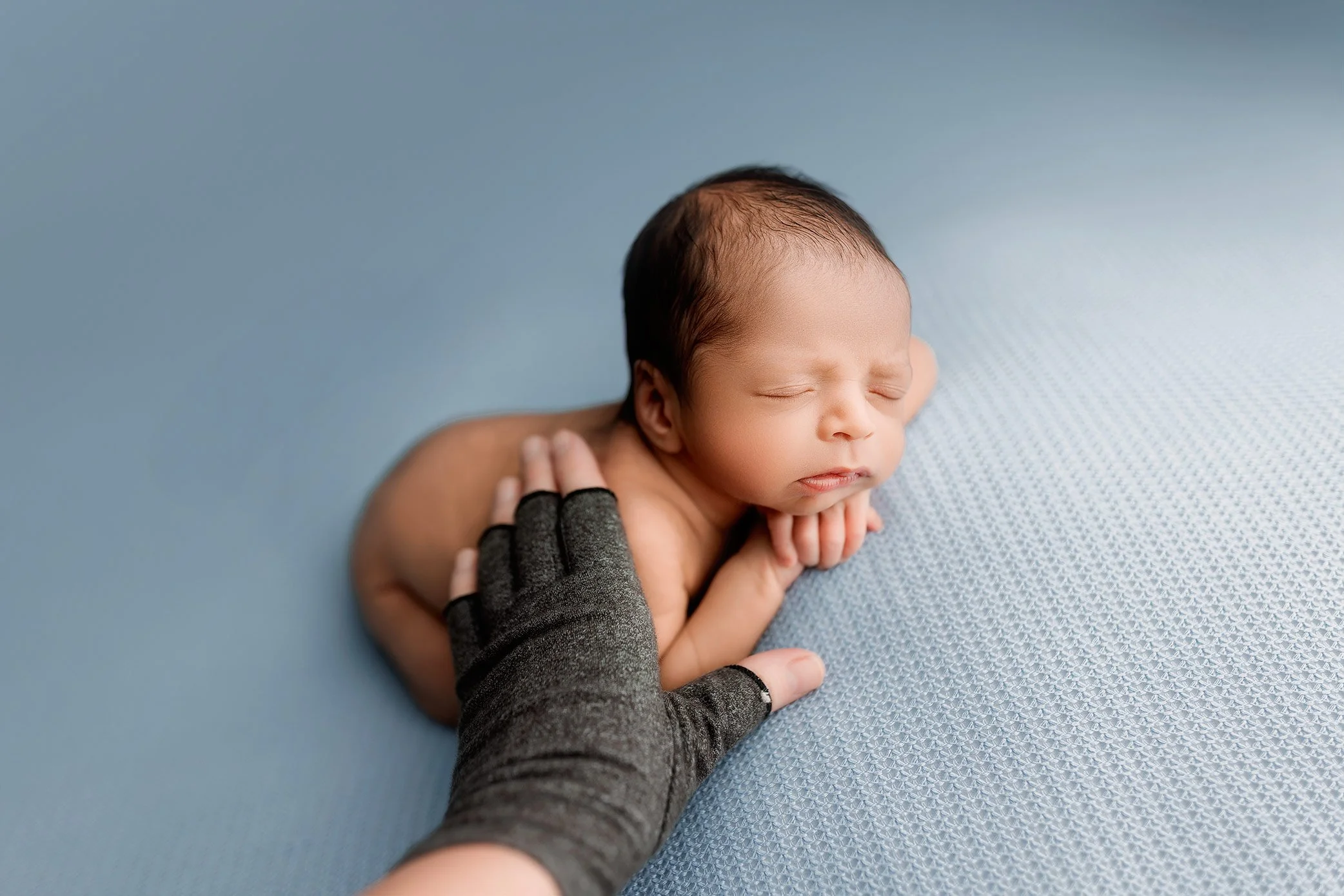 Safely posed newborn resting on hands with photographer support visible