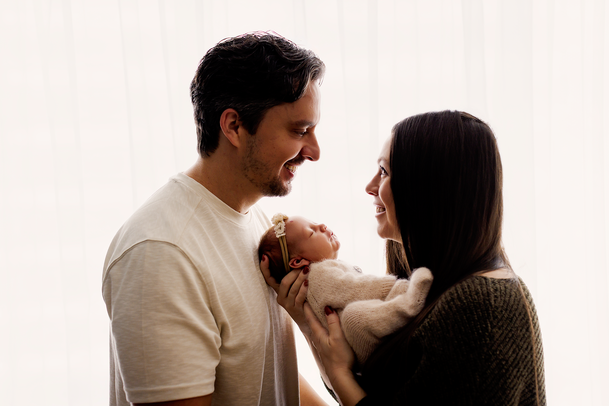 Parents smiling at each other while baby is snuggled in between them.