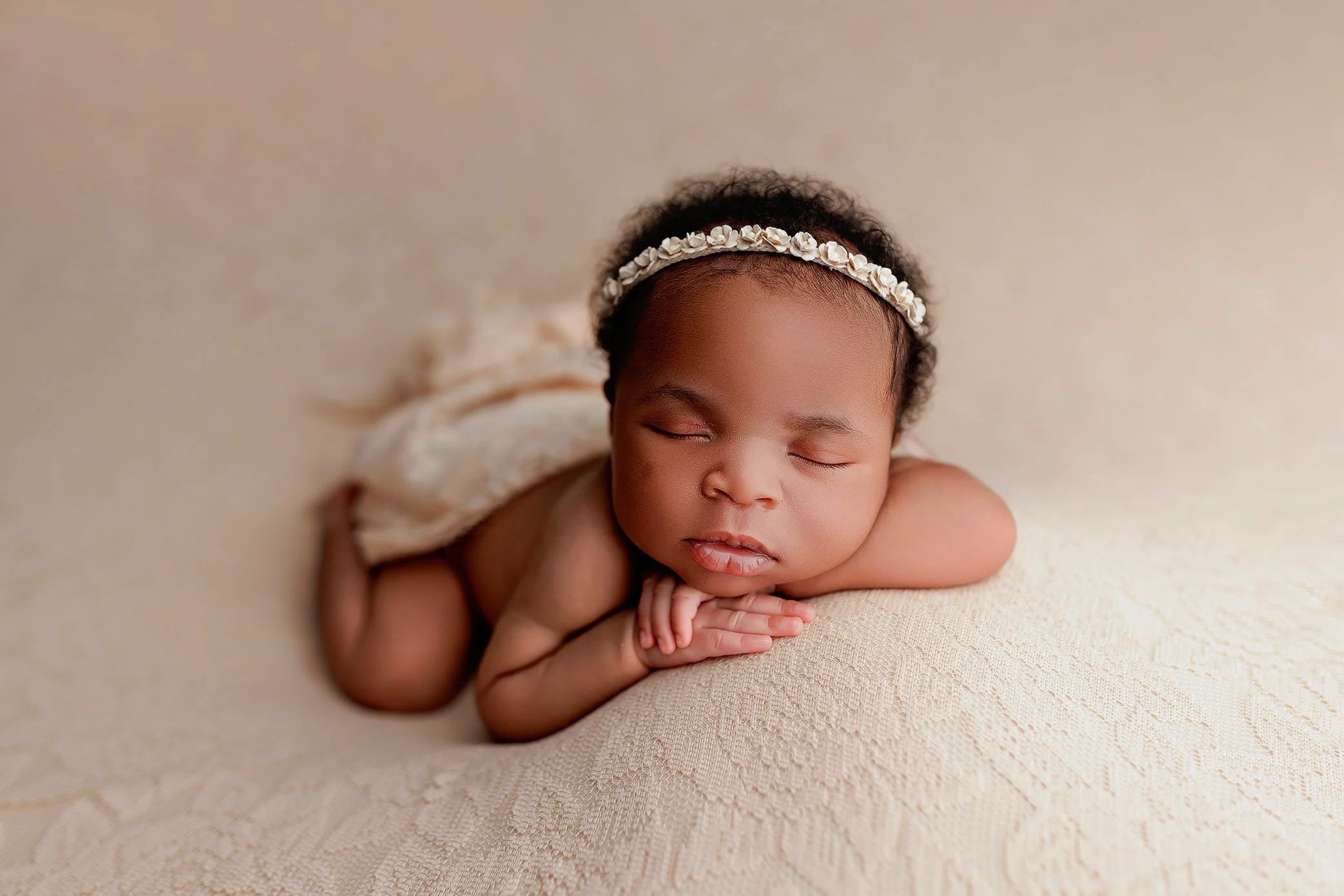 Sleeping newborn baby girl posed on a neutral backdrop during a Salem, Oregon newborn photography session, styled with a delicate floral headband.