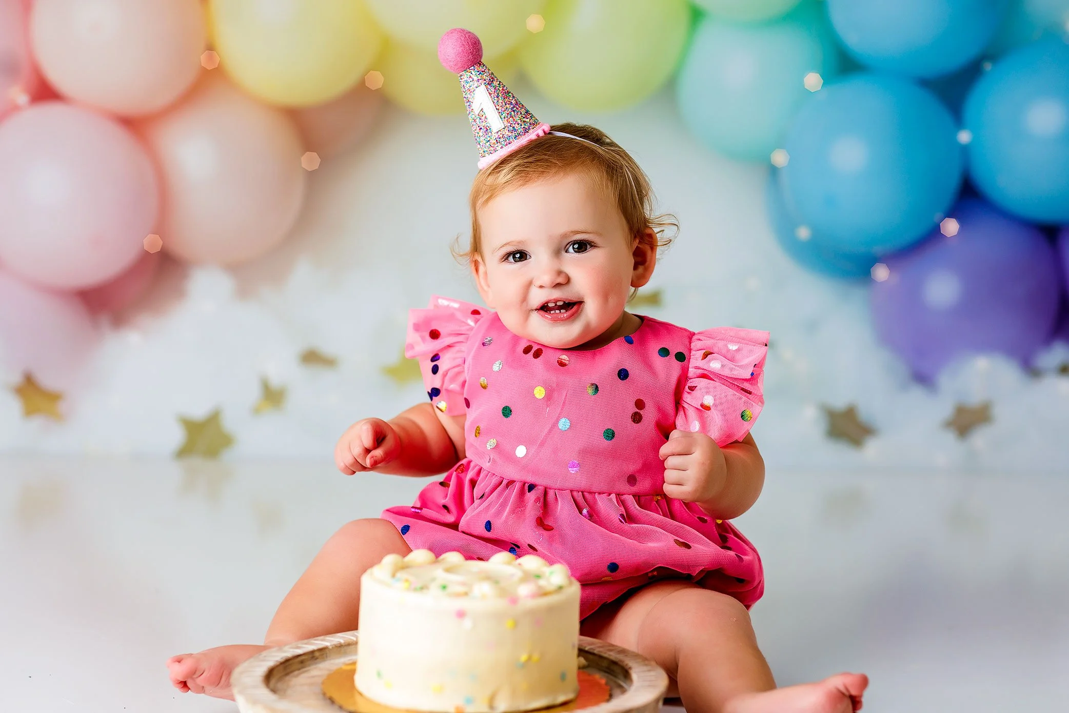 One year old baby girl celebrating with cake smash session, colorful balloons and joyful milestone photography