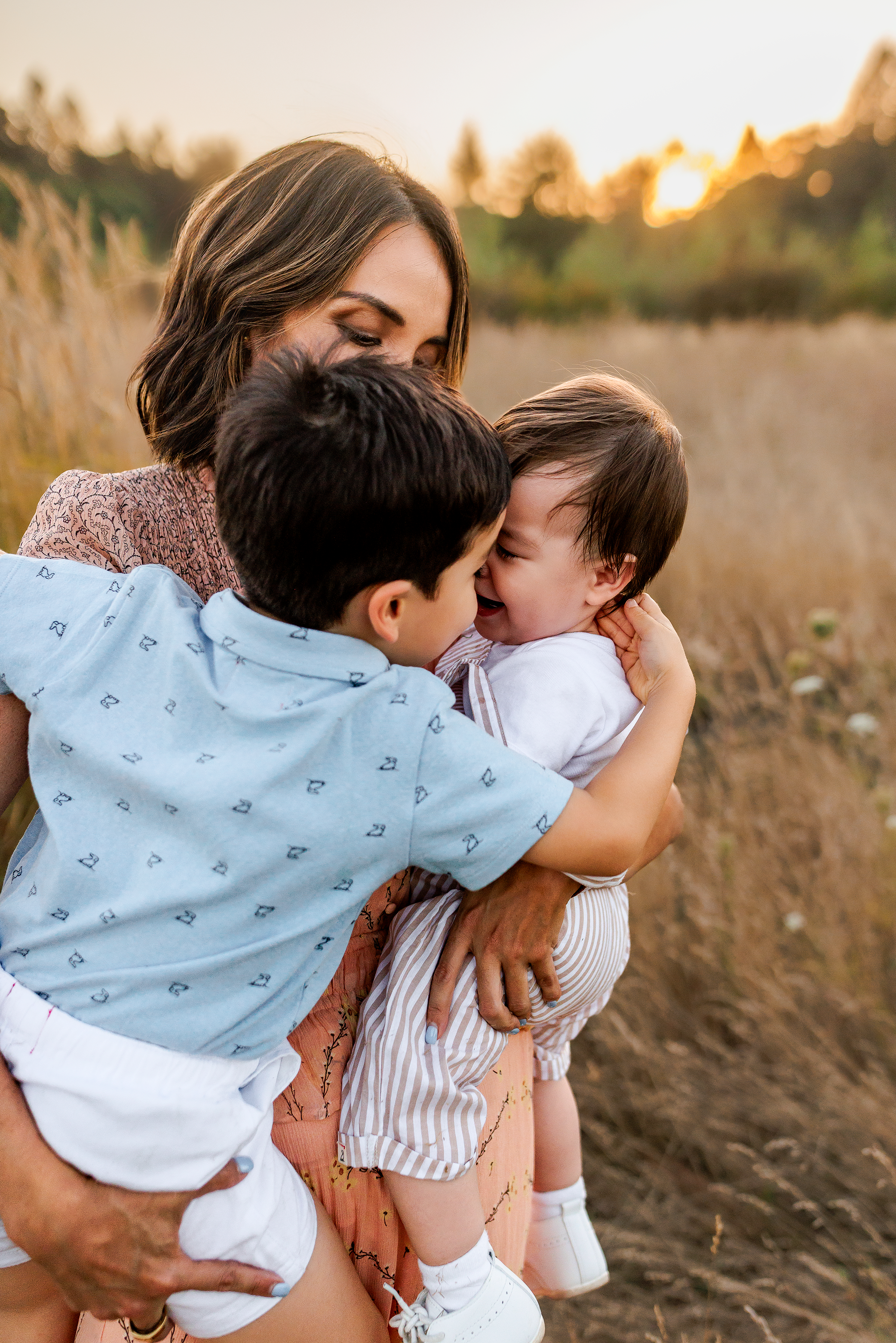 Mother holding two young children hugging and laughing during golden hour family photography session in Salem Oregon