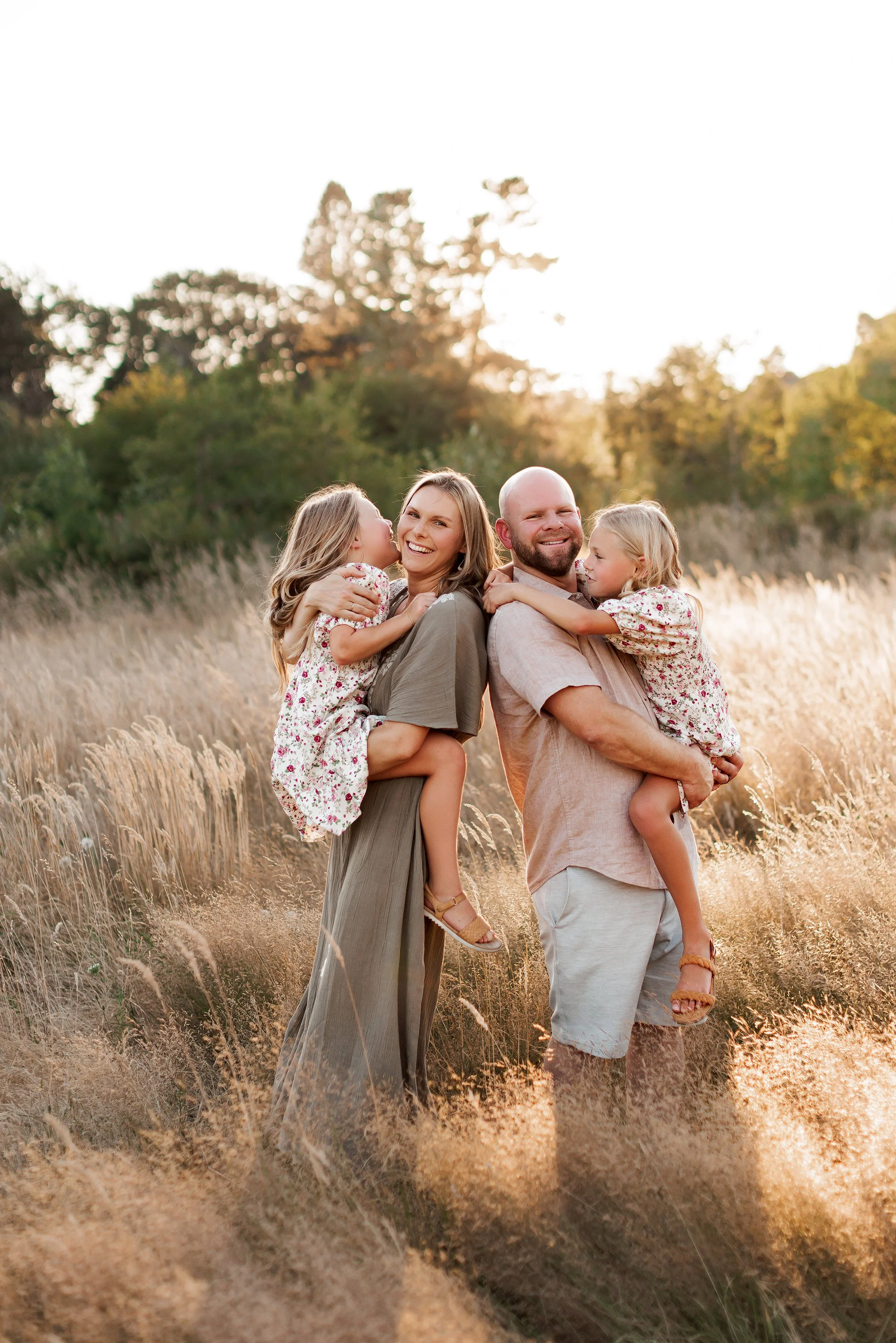 Parents smiling at camera while daughters look away during golden hour family photography session in Salem Oregon field
