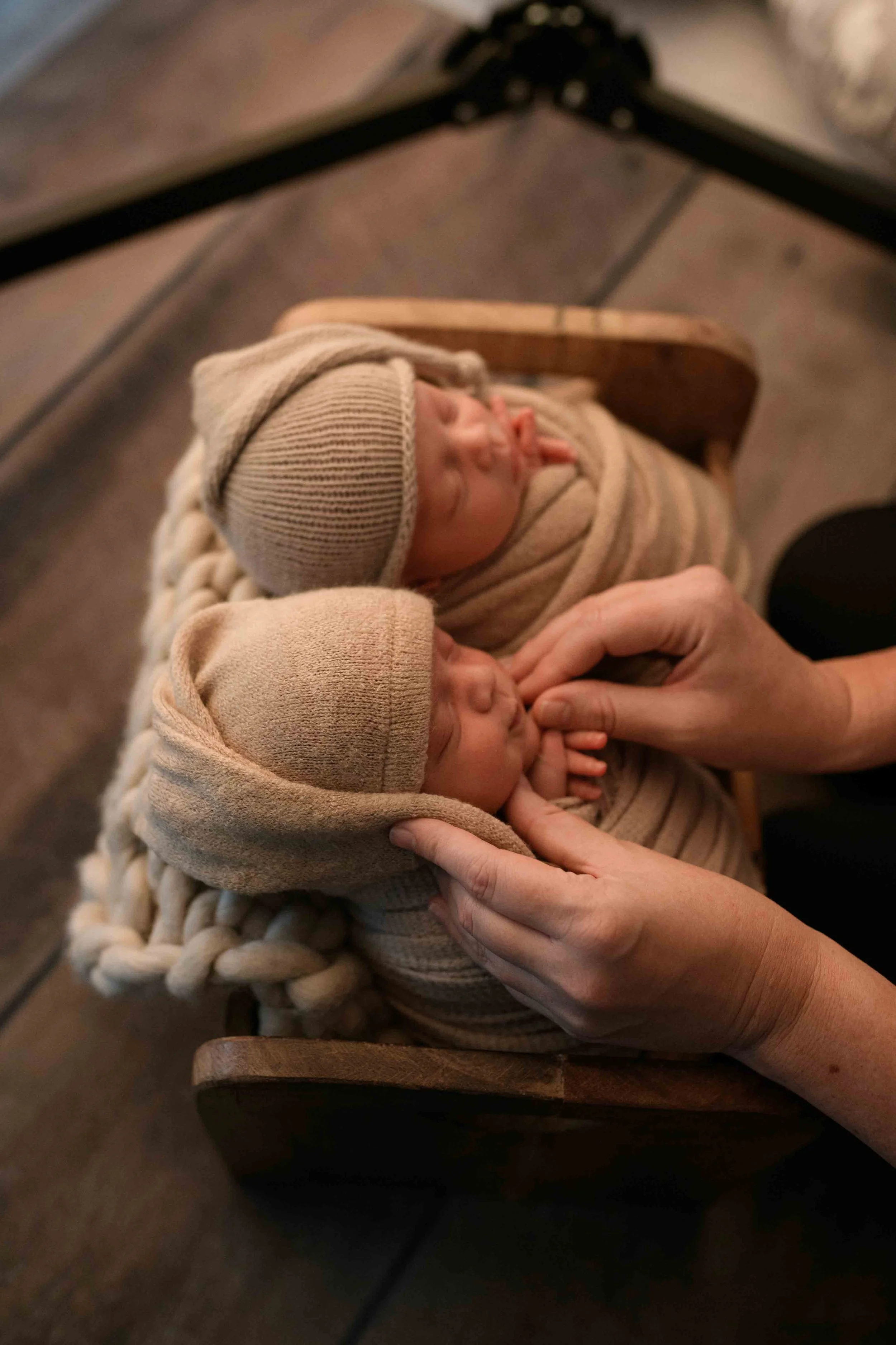 Twin newborn babies wrapped in soft neutral tones while photographer gently adjusts pose, highlighting safe newborn photography in Salem Oregon