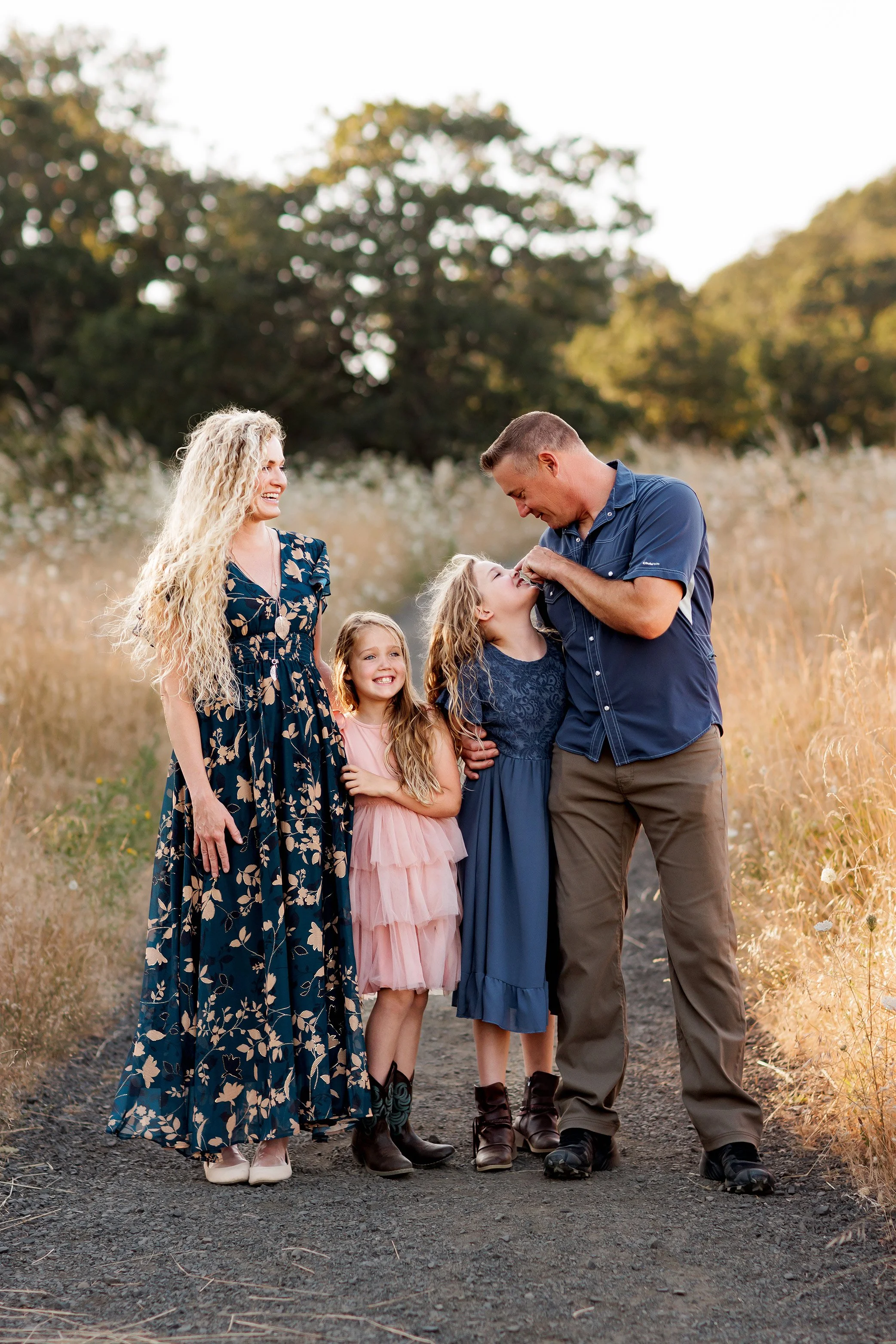 Family of four laughing and looking at each other during playful golden hour outdoor session.