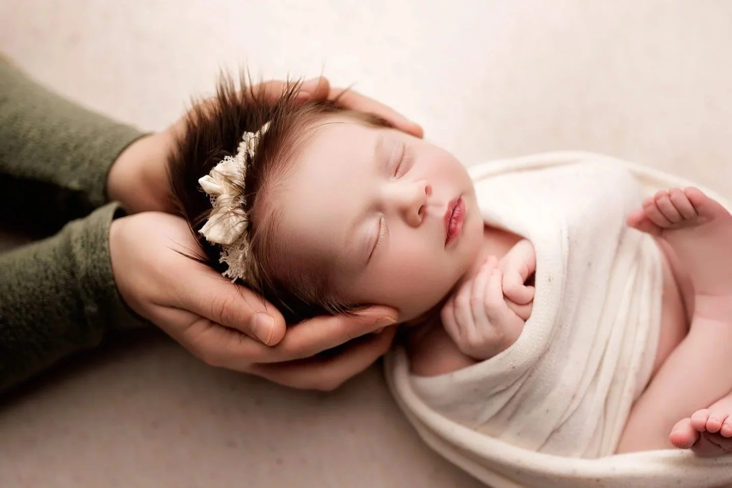 Sleeping newborn baby girl with delicate headband safely supported by her mother's hands.