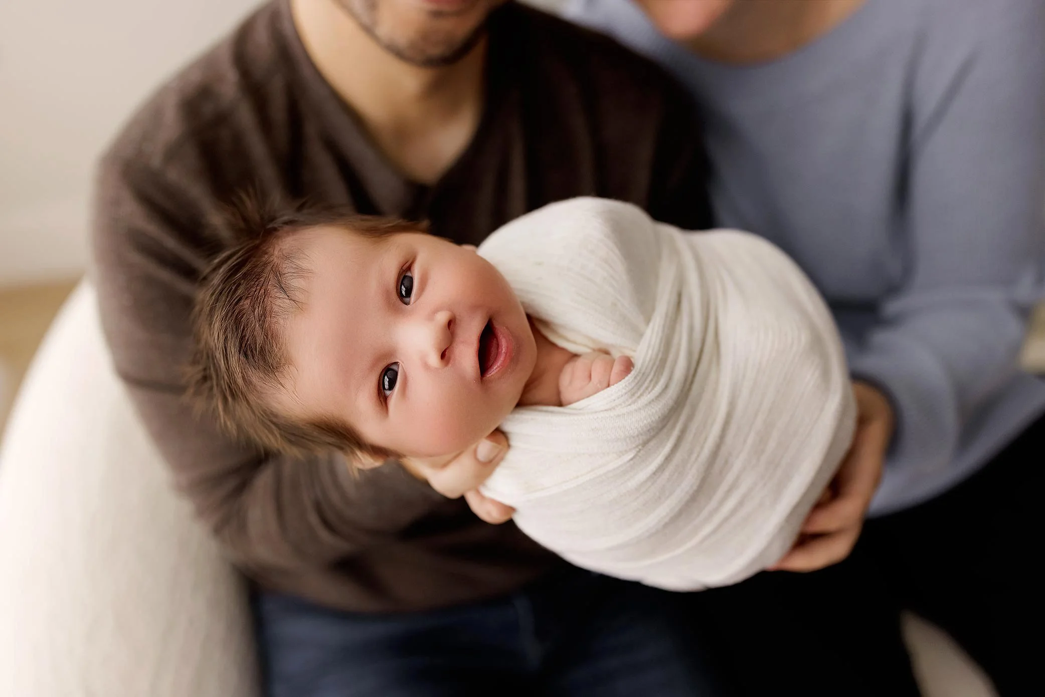 Newborn baby wrapped in a soft blanket looking up while being held in a parent’s arms