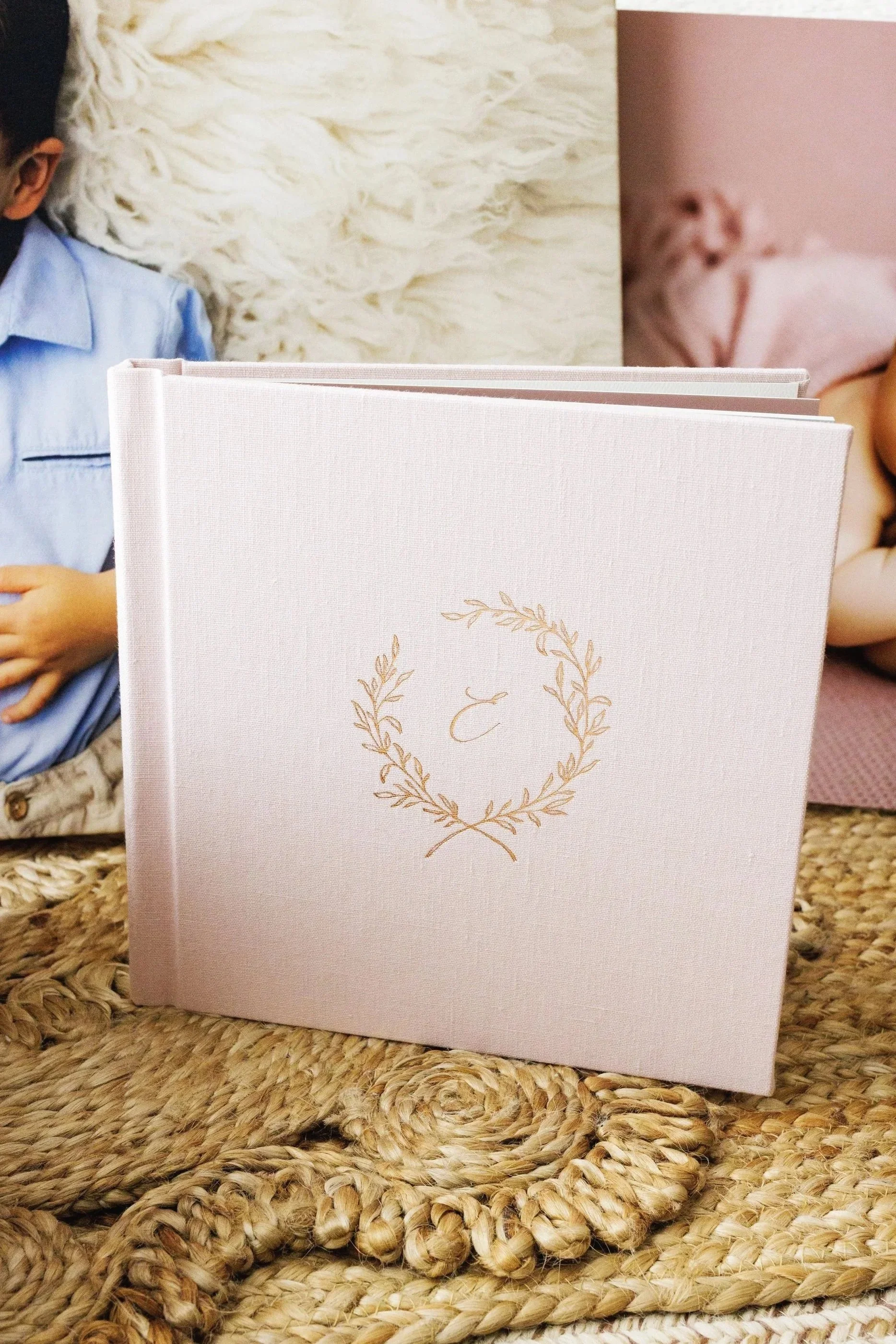 Custom linen newborn photo album with gold embossed wreath displayed with other products in background