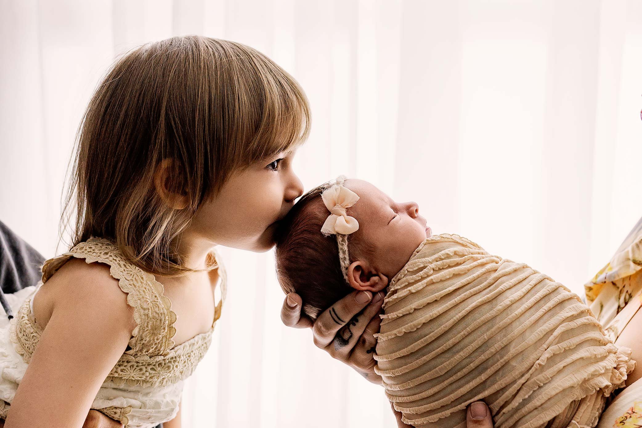 Toddler kissing their newborn sibling during a posed newborn photography session in Salem, Oregon.
