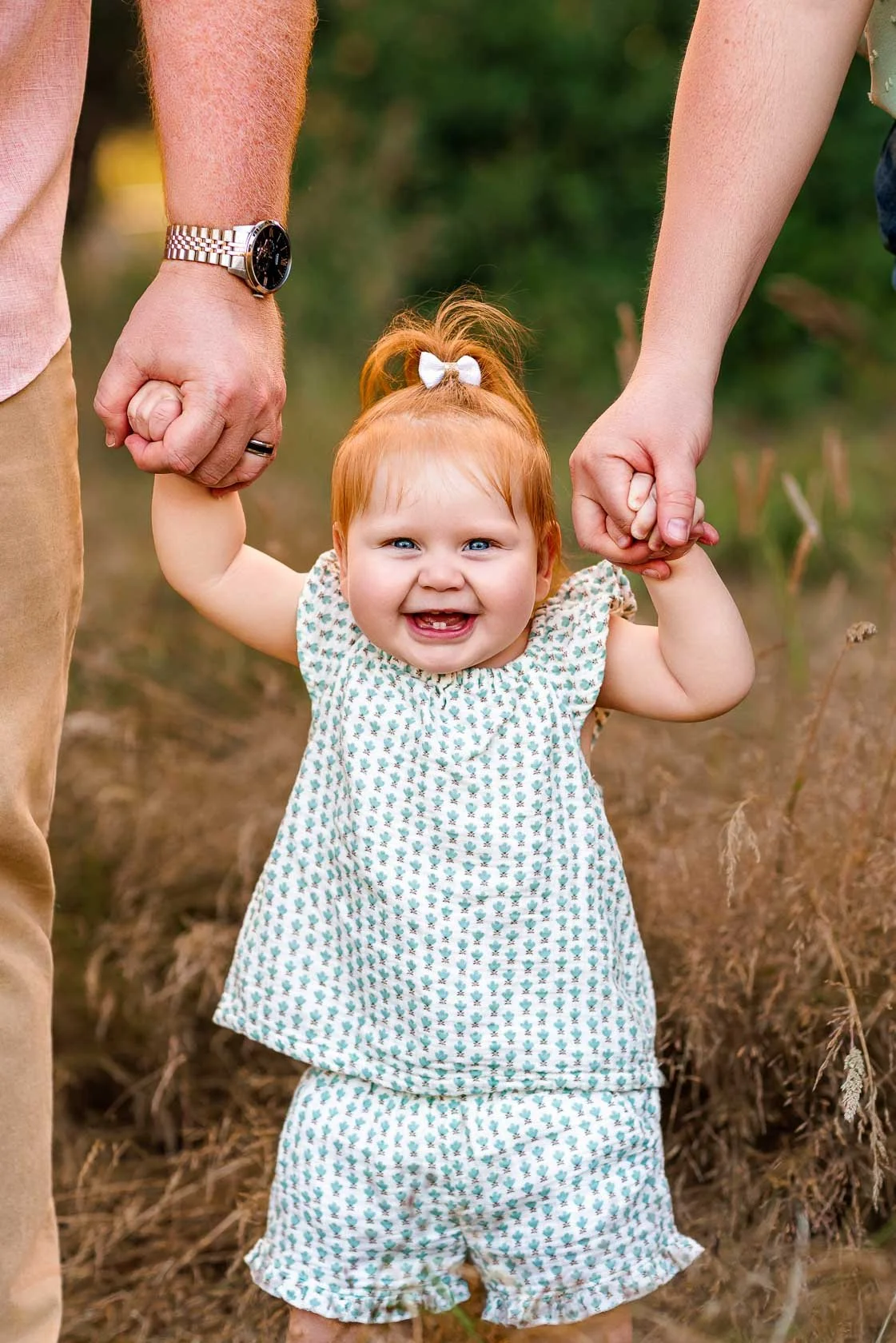 Baby taking first steps while holding both parents' hands during an outdoor baby milestone photography session in Salem, Oregon.
