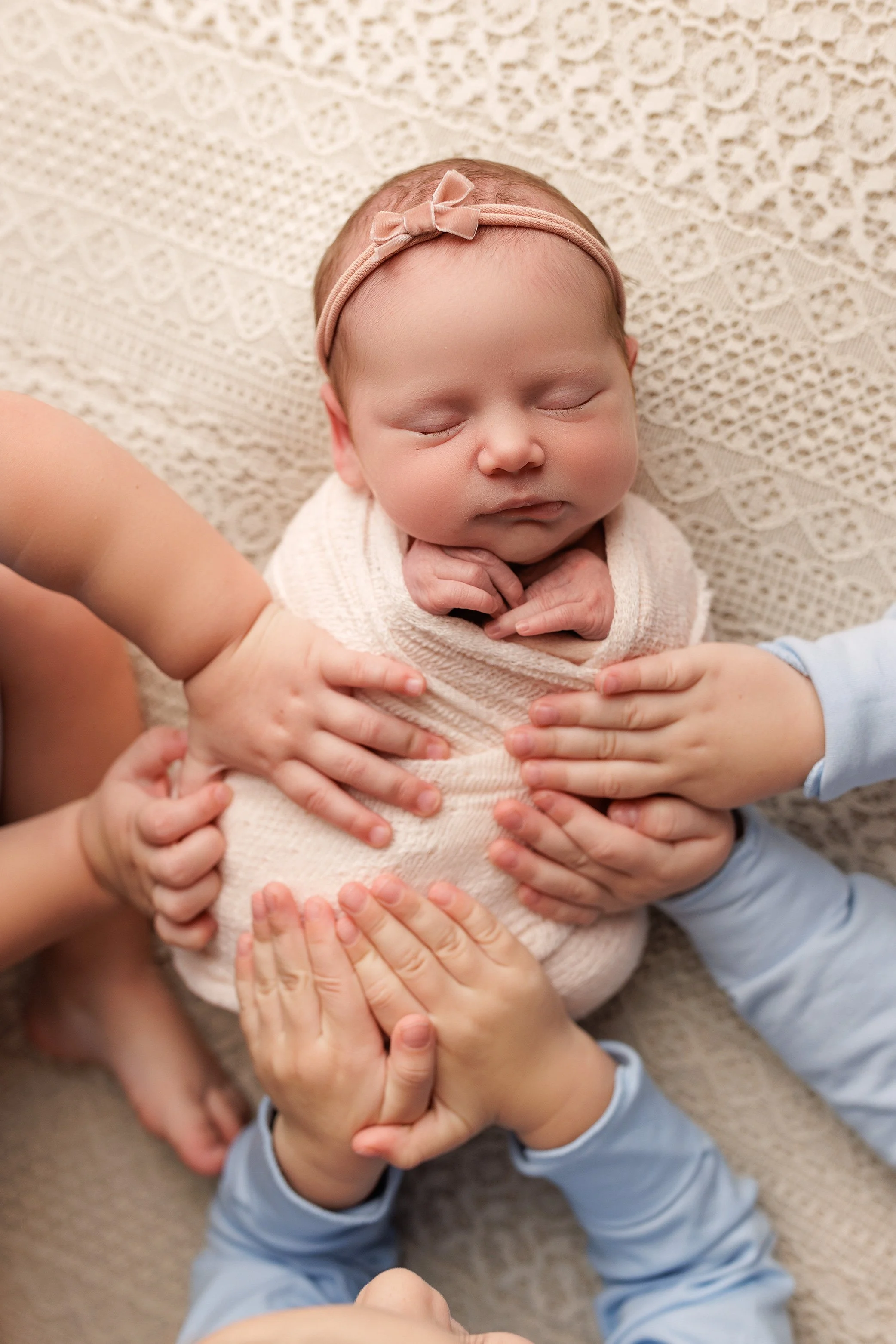Multiple siblings’ hands gently resting on a swaddled newborn baby during a Salem, Oregon newborn photography session, highlighting connection and tenderness.