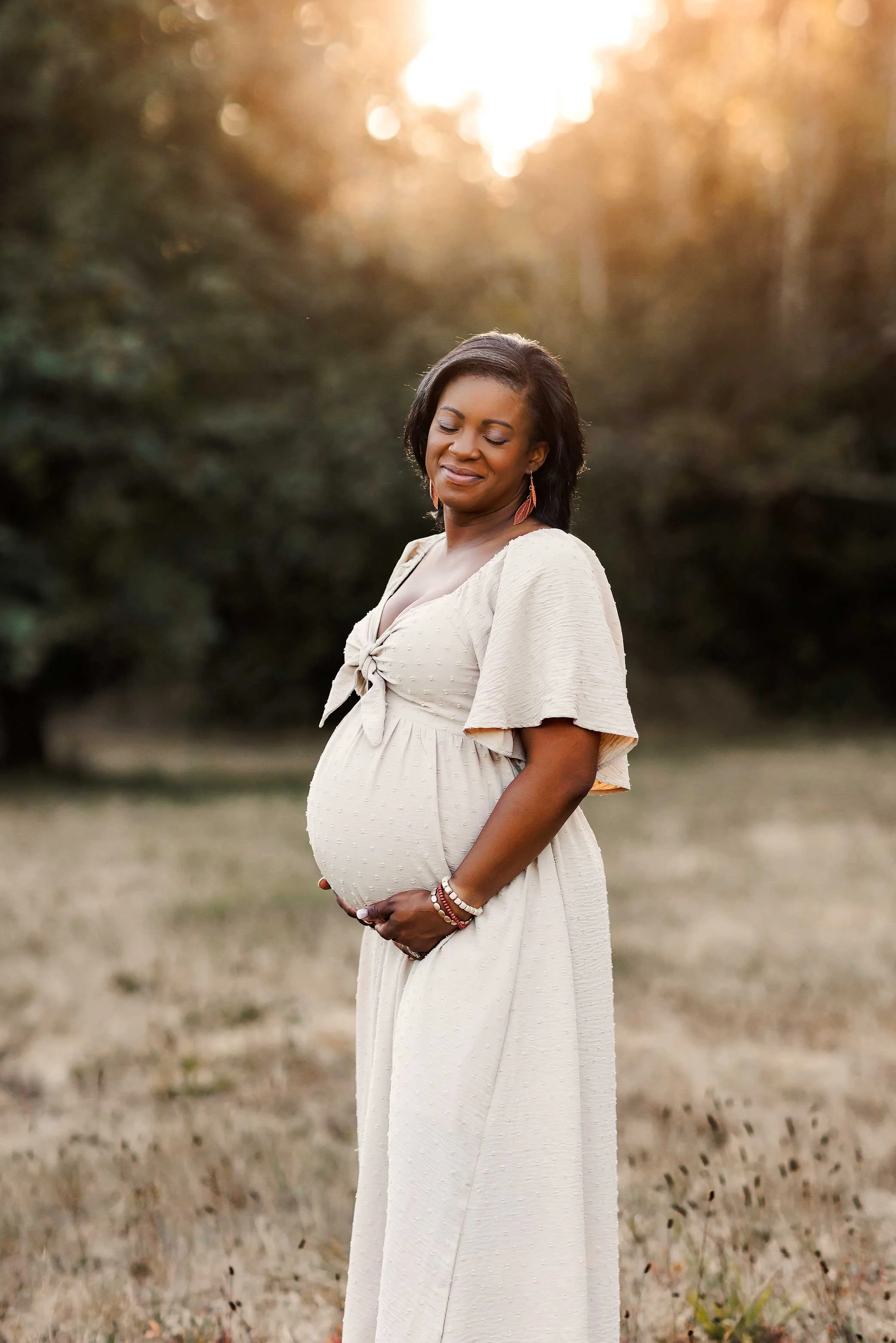 Pregnant woman in neutral dress holding belly outdoors, soft golden light maternity portrait in Salem Oregon