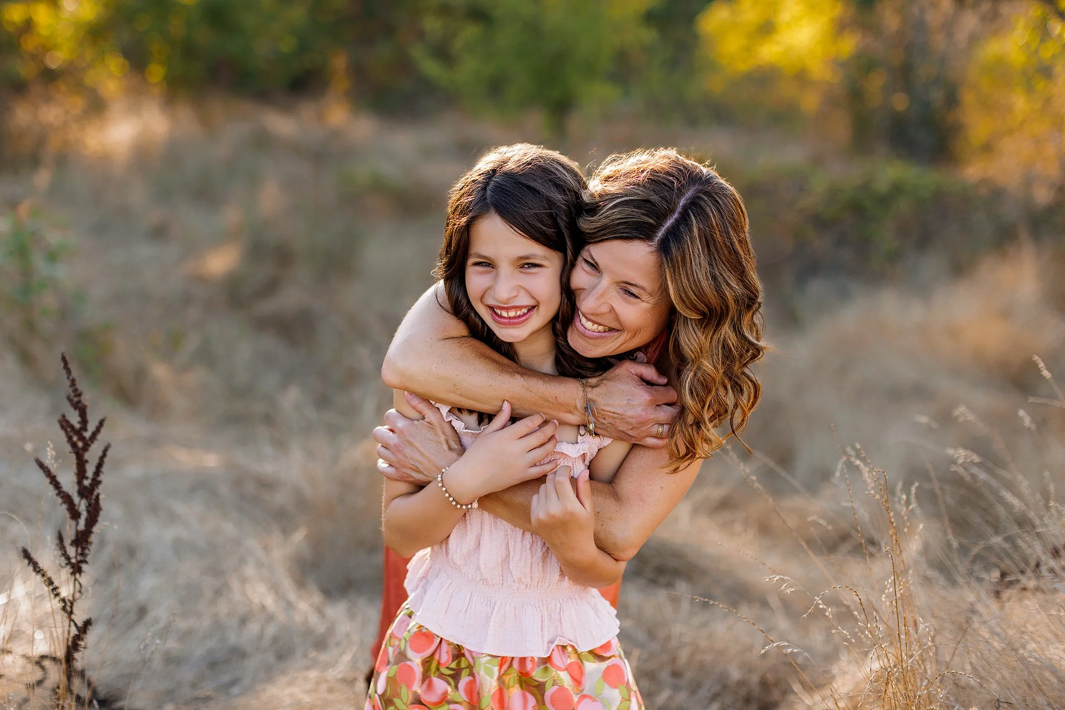 Mother hugging smiling daughter in a golden field at sunset in Salem, Oregon during a family session.