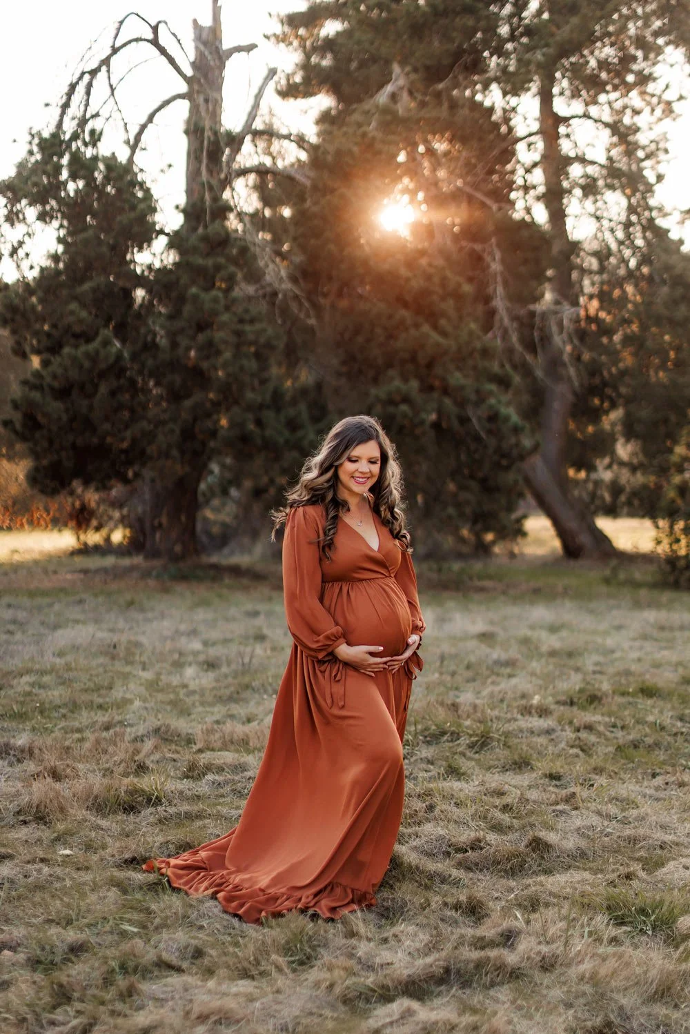 Pregnant mother in rust dress standing in open field during sunset maternity session in Salem Oregon