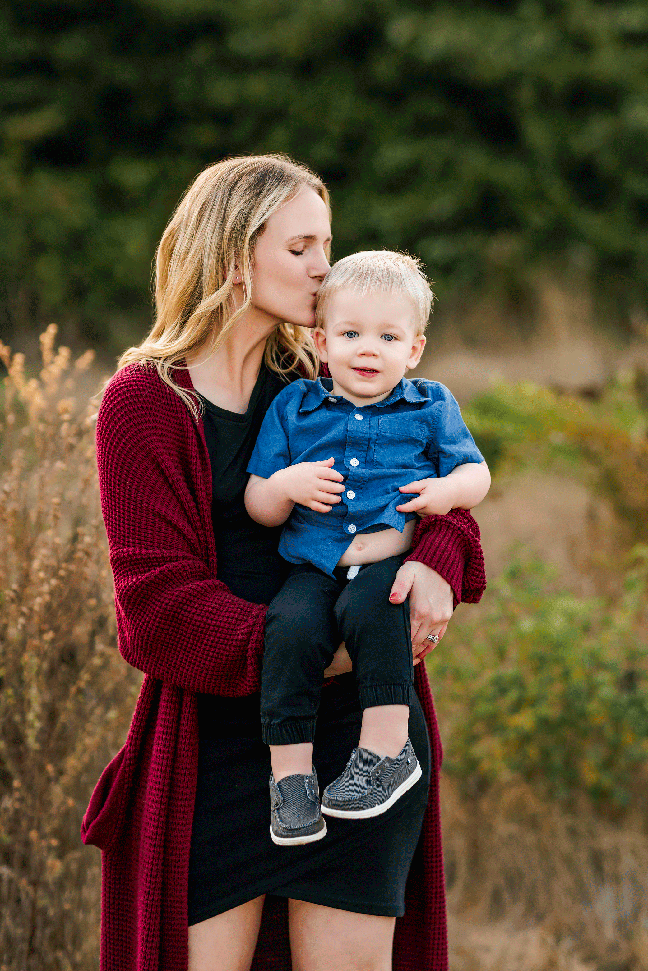 Pregnant mom kissing toddler son on the head during outdoor family photography session in warm evening light.