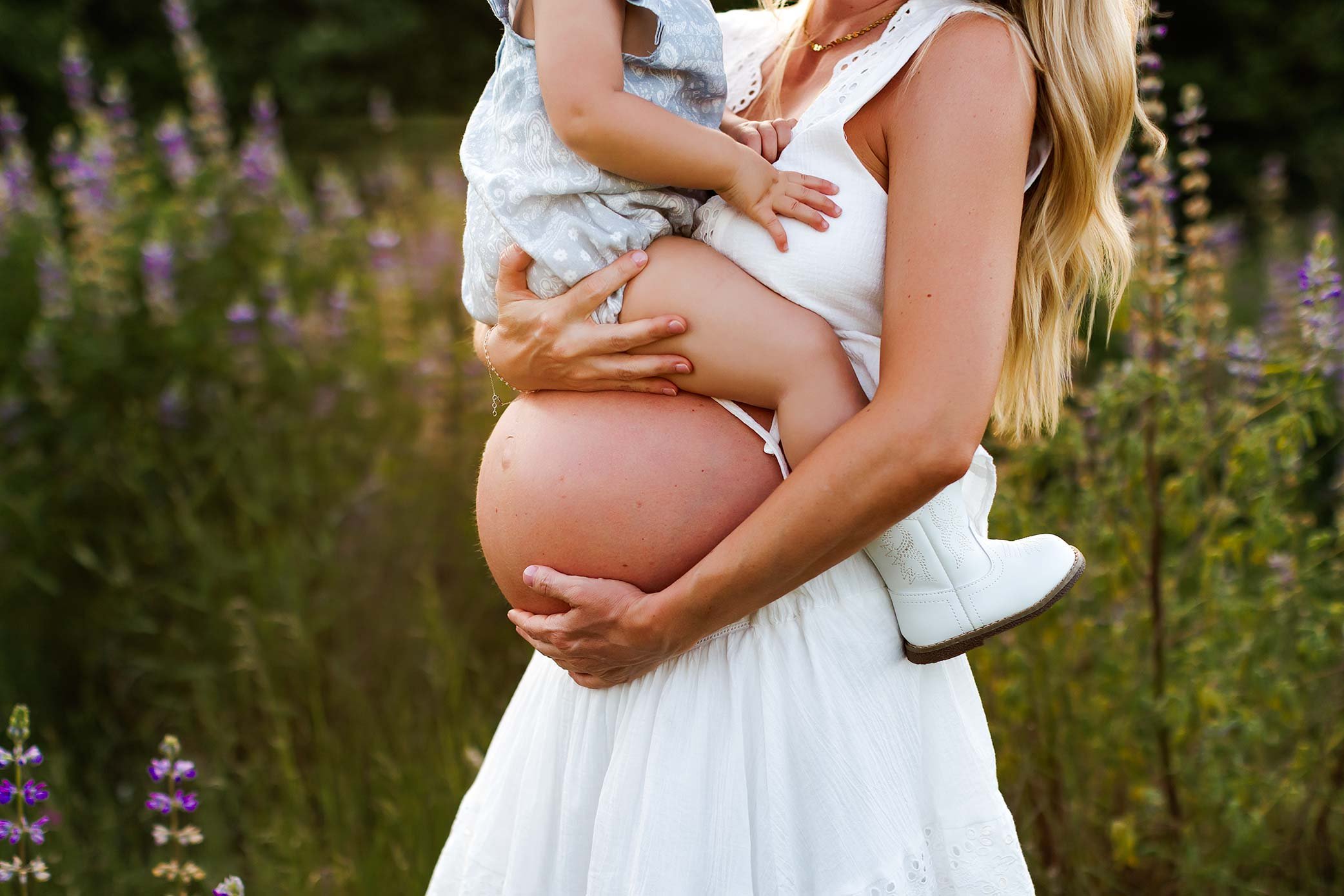 Pregnant mother holding her toddler while cradling her baby bump during an outdoor maternity session.