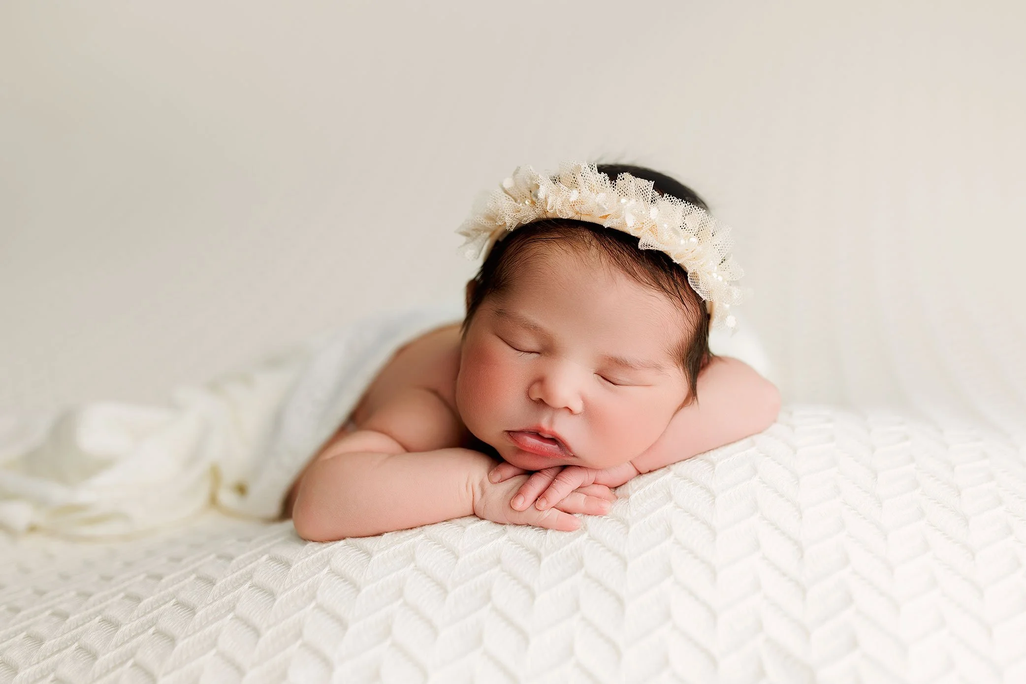 Newborn baby girl posed on cream blanket with headband during studio newborn photography session near Portland Oregon