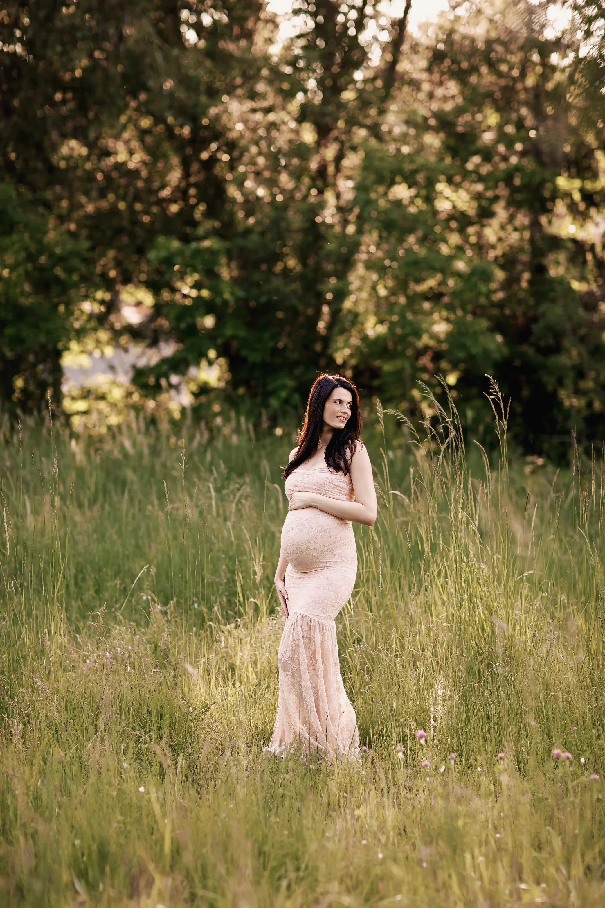 Expecting mother in blush dress standing in tall grass during outdoor maternity session in Salem Oregon