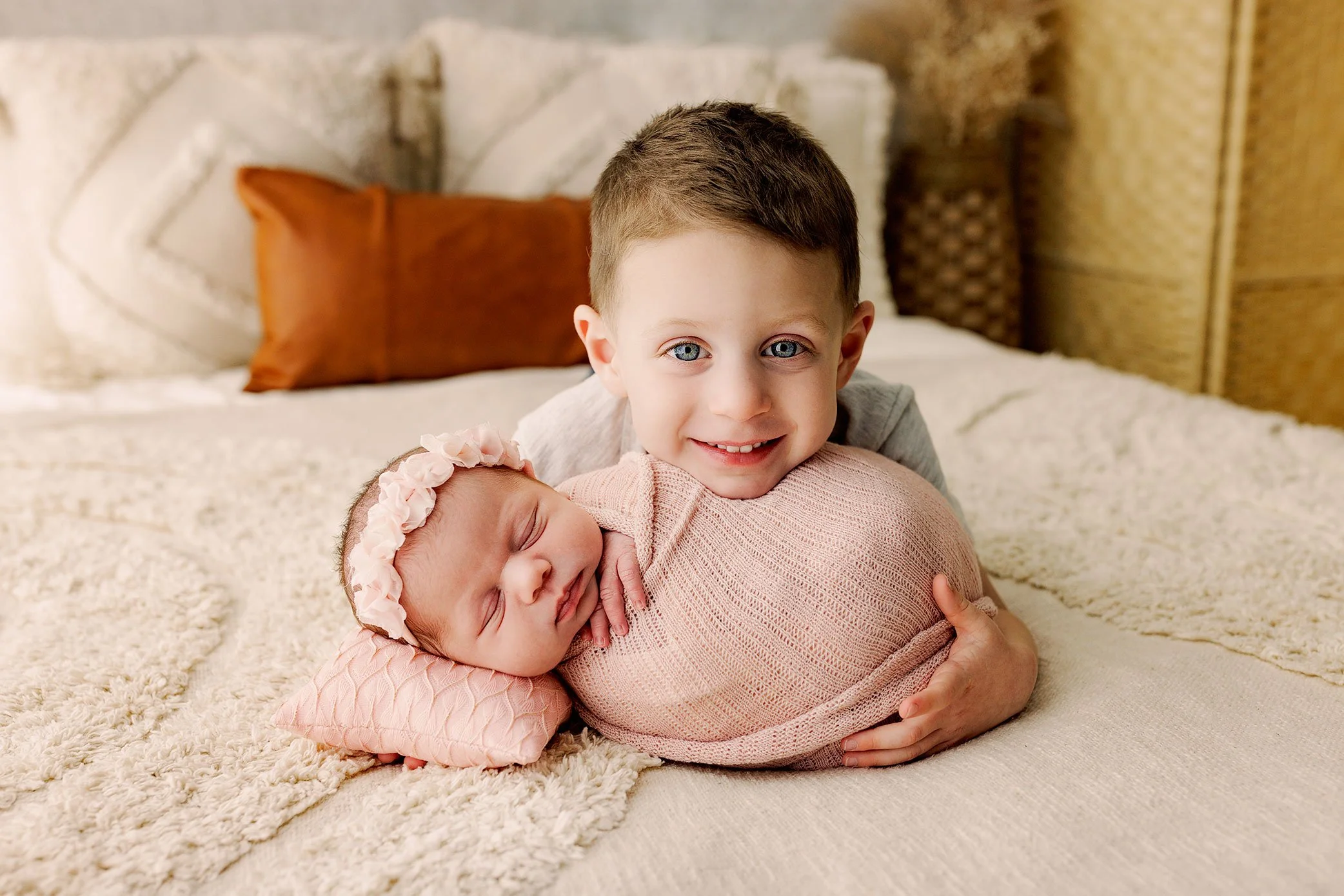 Older sibling gently hugging a swaddled newborn baby during a Salem, Oregon newborn photography session in a light, neutral studio setting.