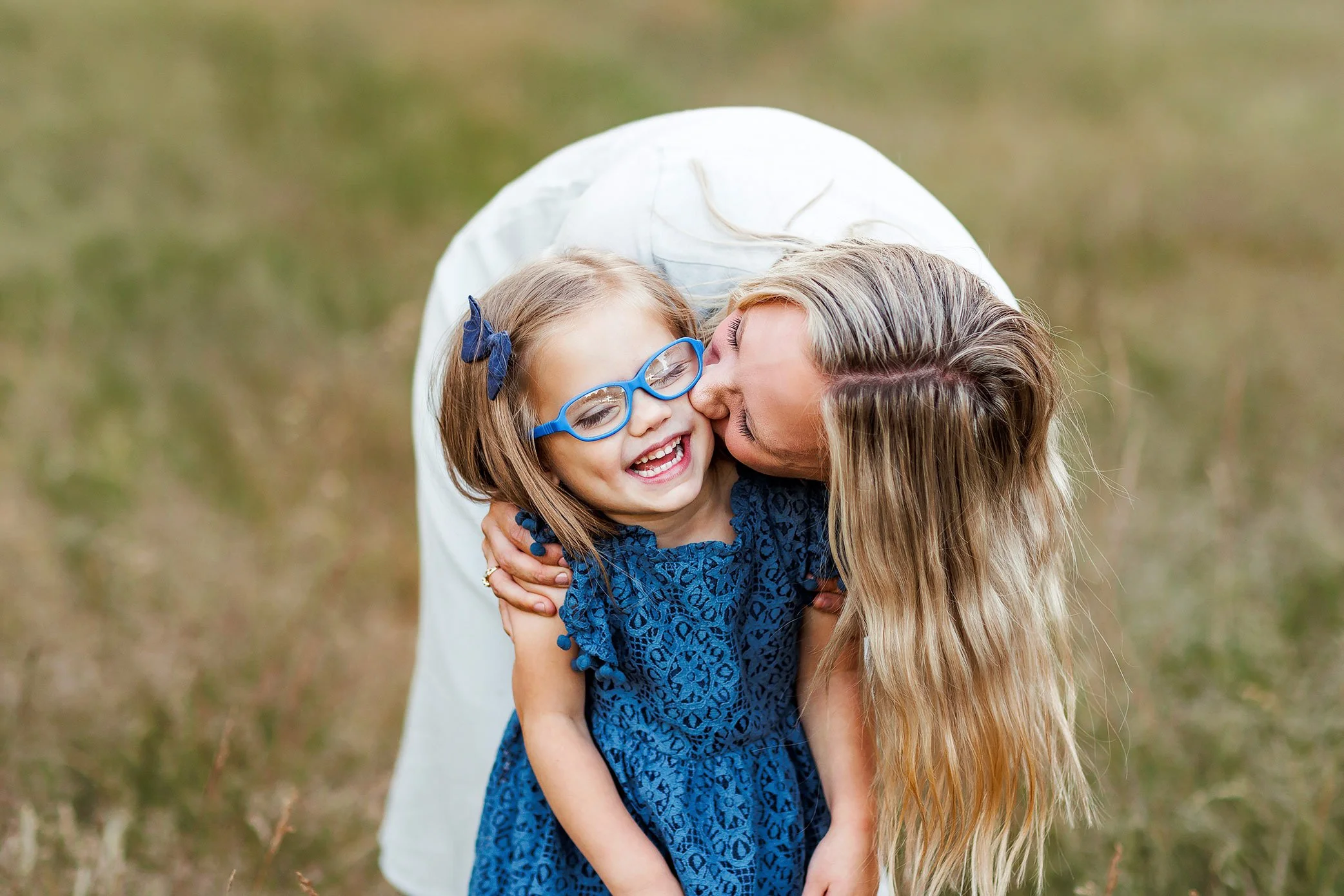 Mother kissing her laughing daughter wearing blue glasses during a Salem, Oregon family portrait session.