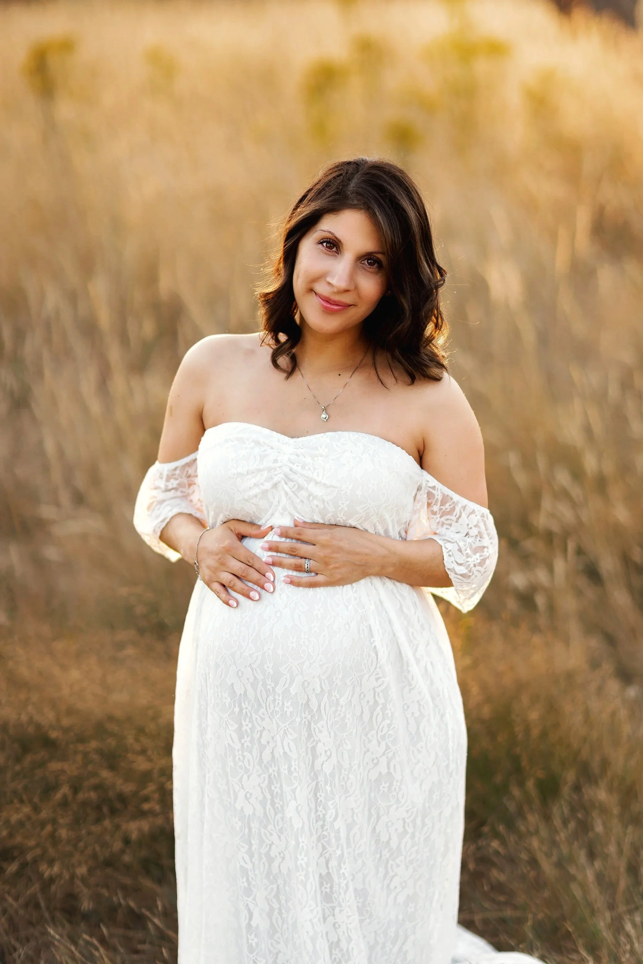 Pregnant mother holding belly in golden field during outdoor maternity photography session in Salem Oregon