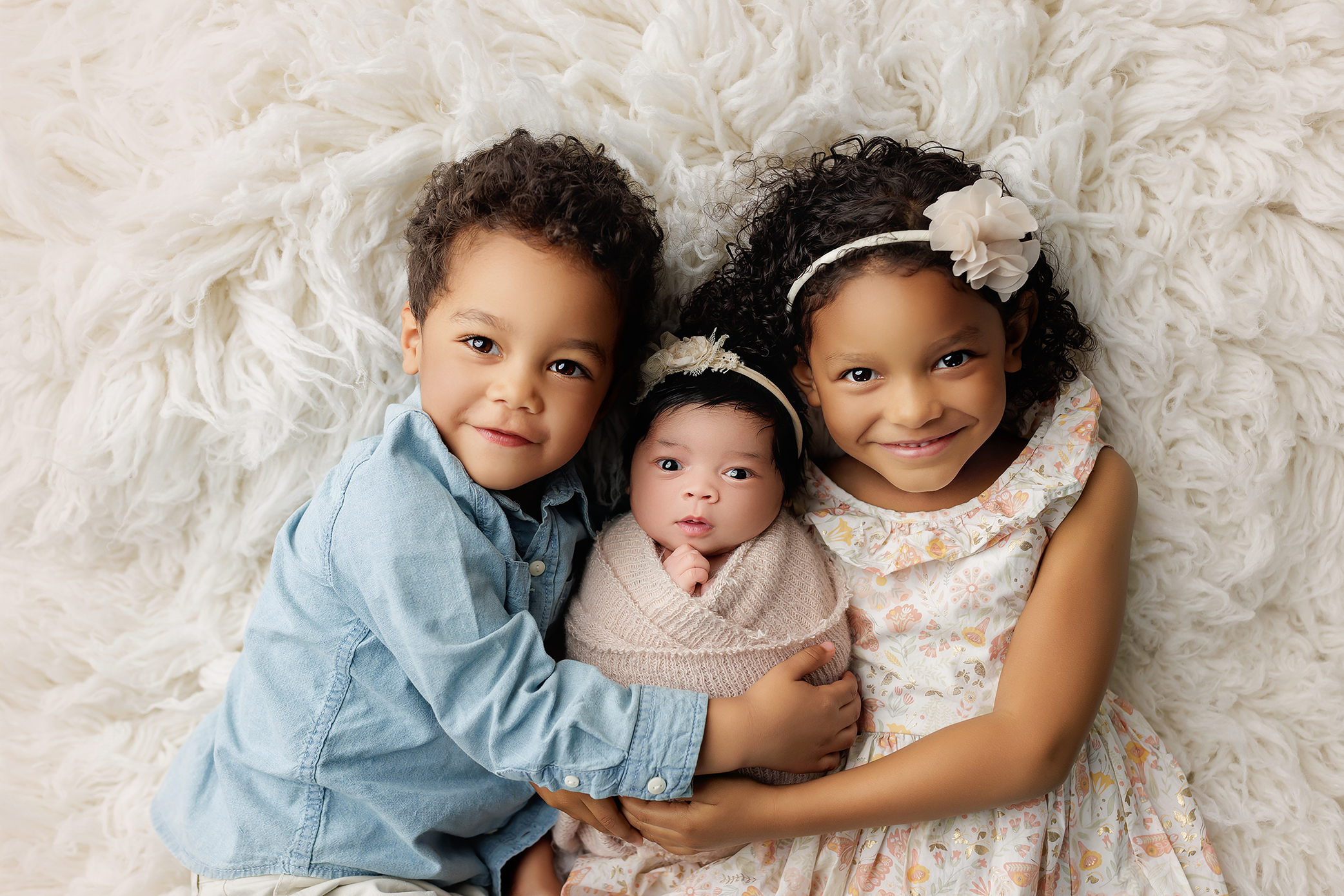 Three siblings gently holding their newborn baby during a studio newborn photography session in Salem, Oregon.