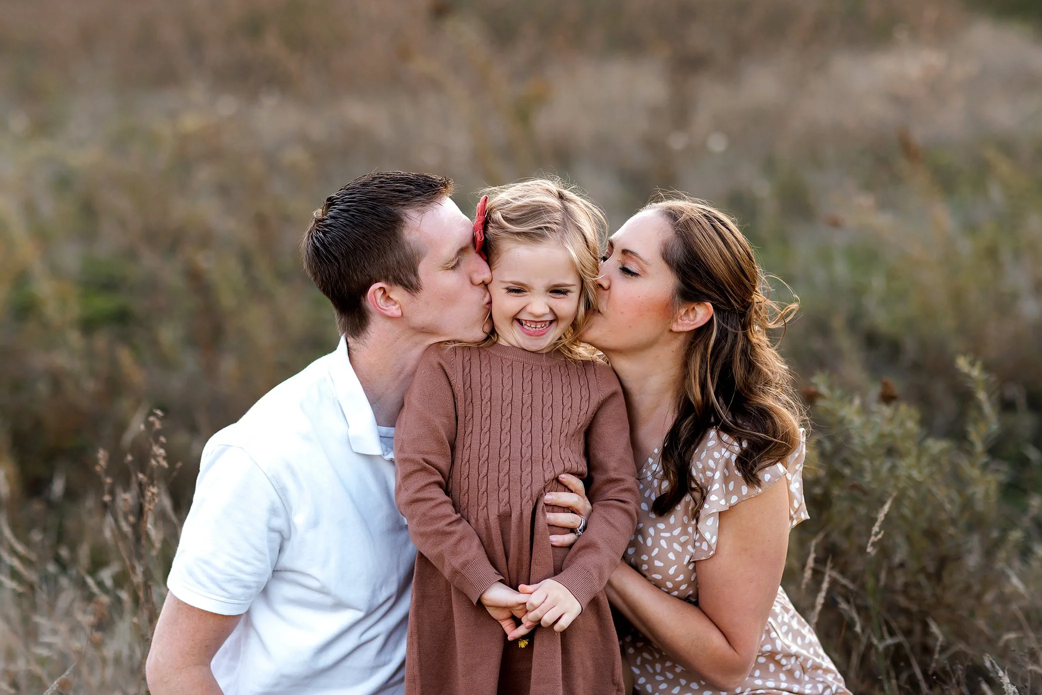 Parents kissing their daughter on the cheeks during an outdoor family photography session in Salem, Oregon.