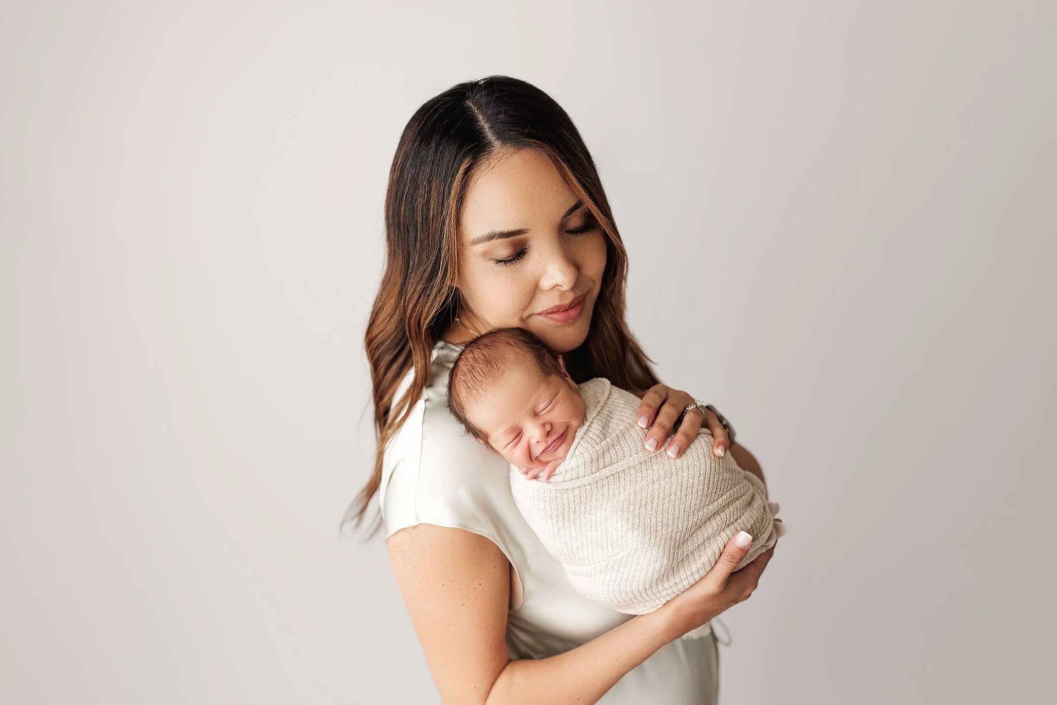 Mother smiling down at her swaddled newborn baby during studio portrait session.