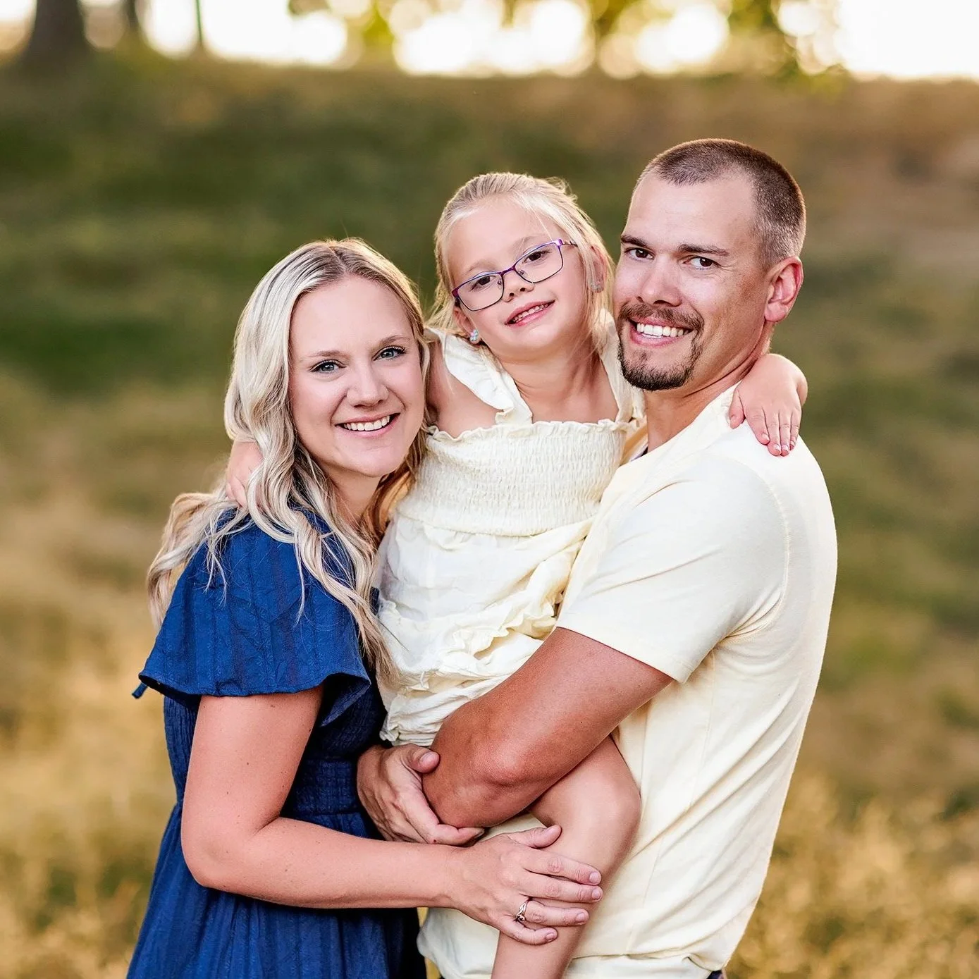 Parents holding daughter between them during outdoor golden hour family photography session.