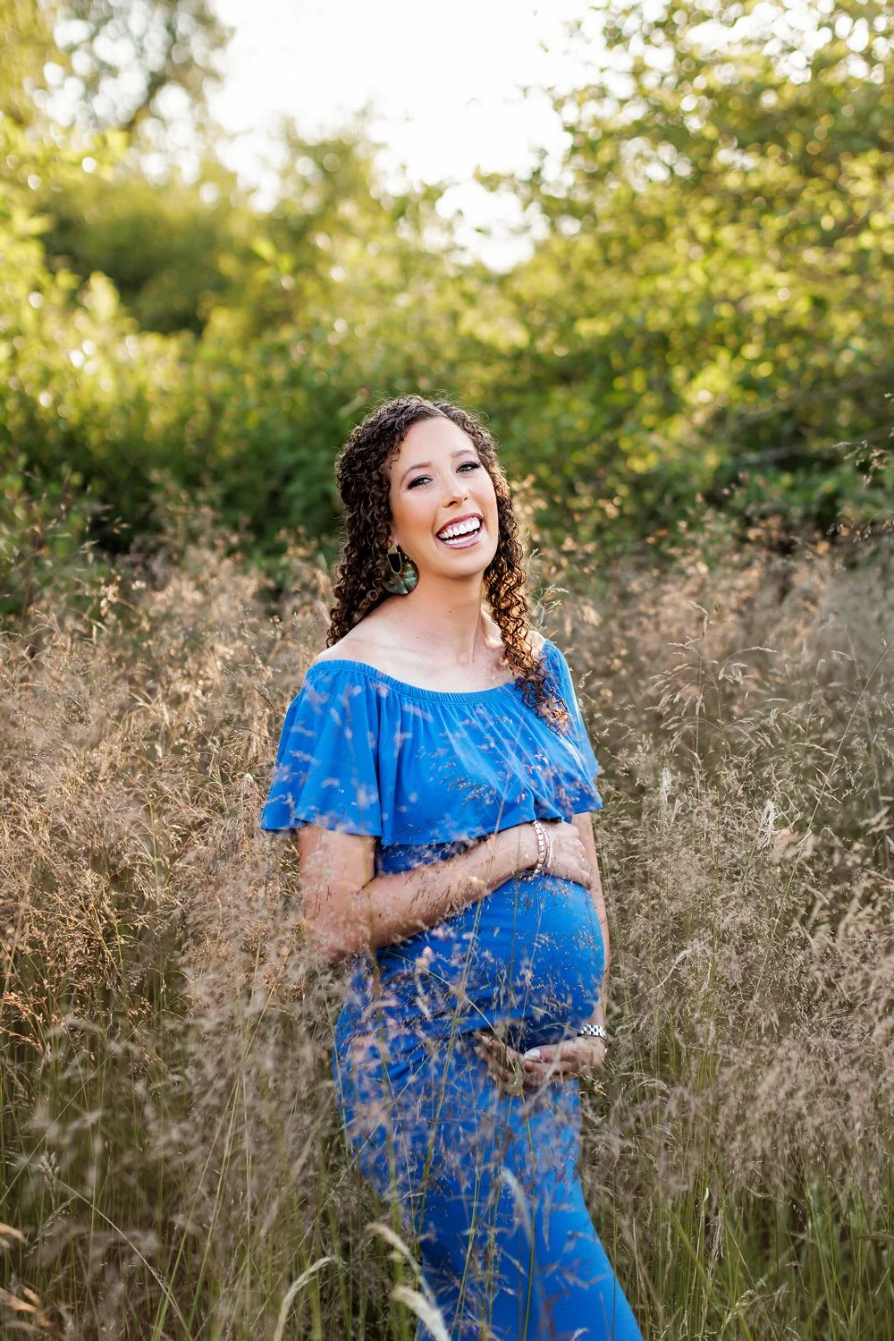 Expecting mother in blue dress smiling in tall grass during outdoor maternity session in Salem Oregon