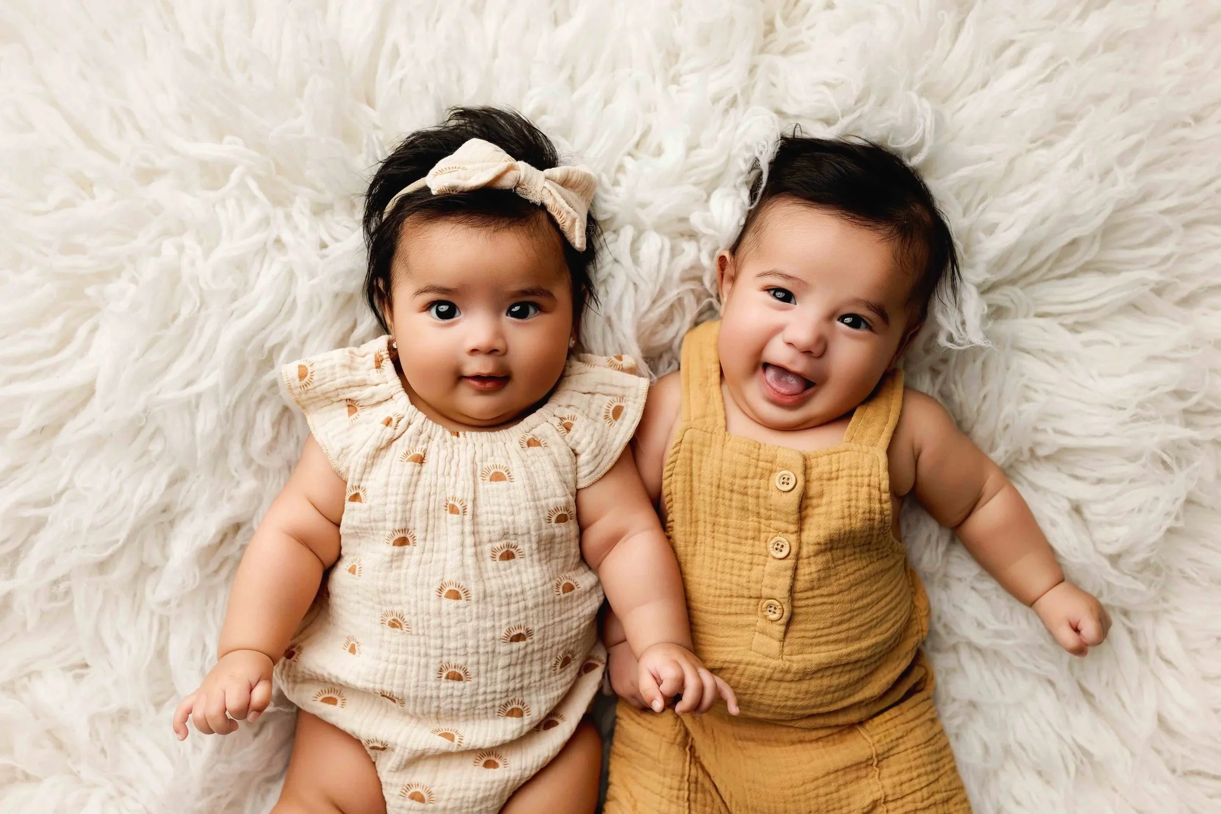 Twin babies smiling during 3 month baby milestone photography session, capturing early sitting stage with soft neutral styling