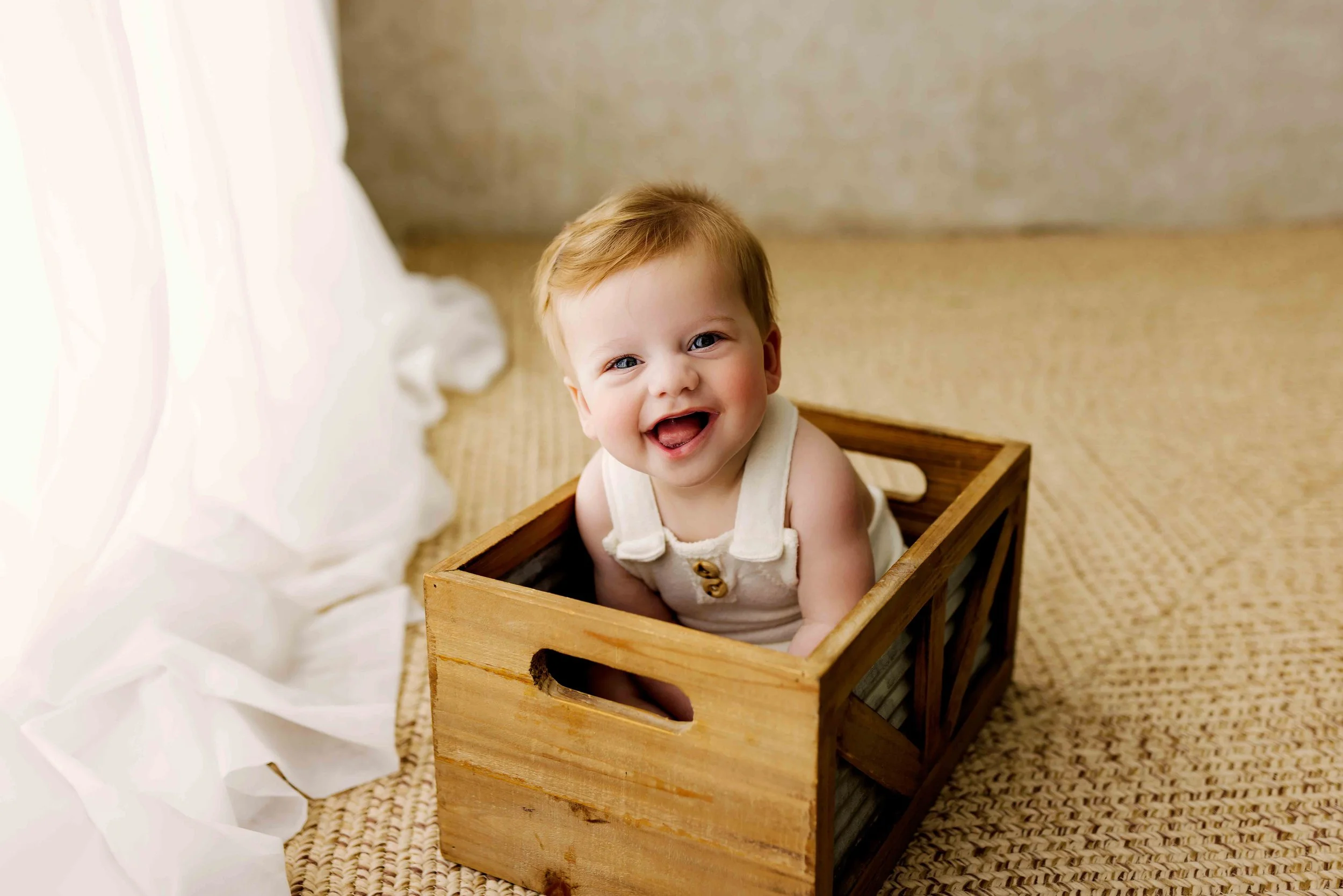 Smiling baby sitting in wooden crate during milestone session in Salem Oregon, capturing personality and natural expressions