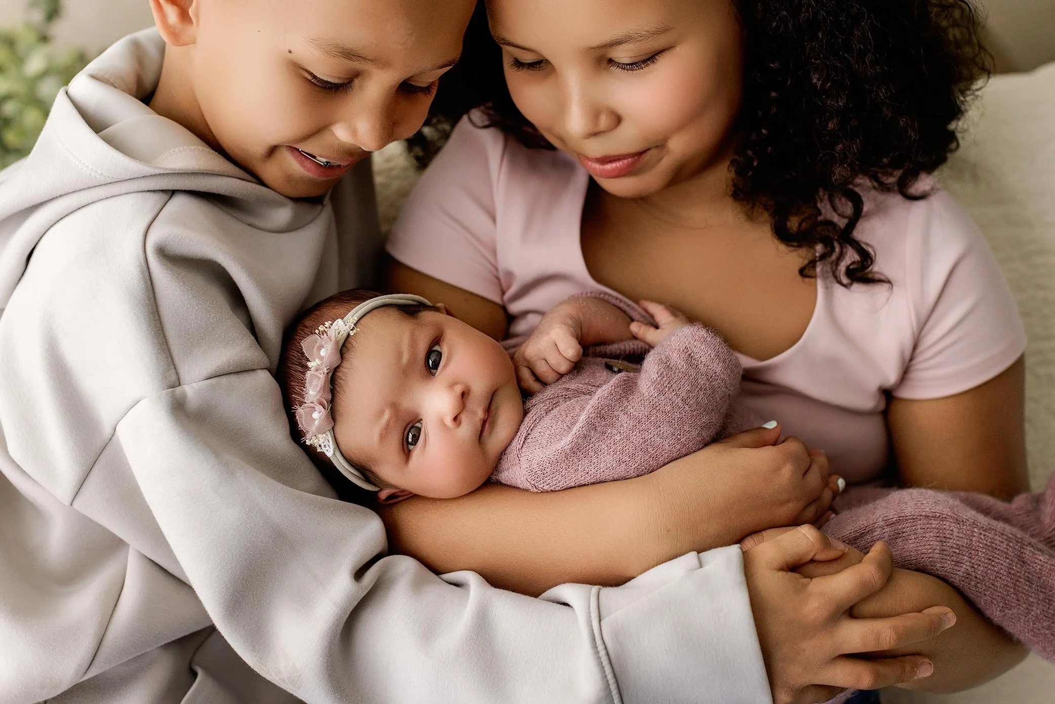 Brother and sister cuddling their newborn sibling during a family newborn photography session.