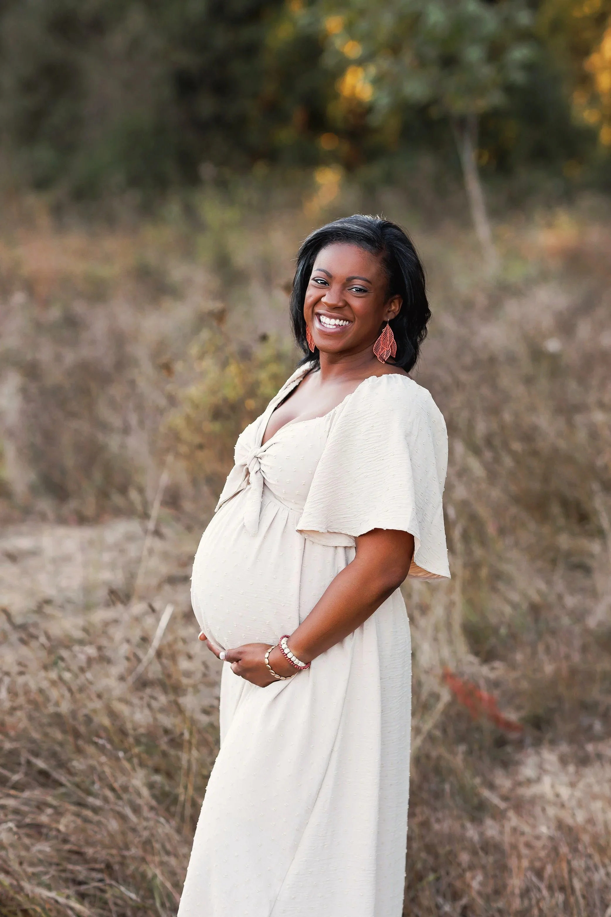Pregnant mother in cream dress smiling during outdoor maternity session in Portland Oregon