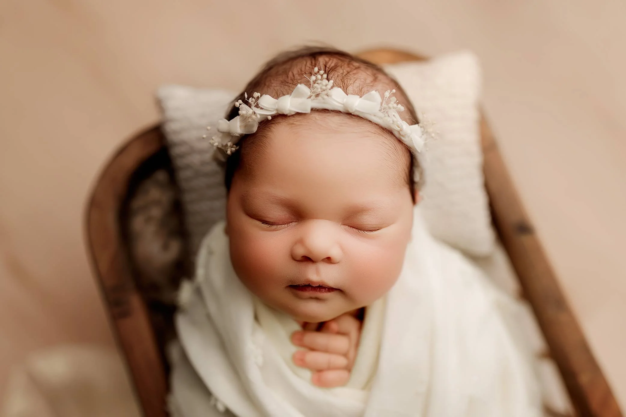 Newborn wrapped pose photographed on a cozy newborn bed prop.