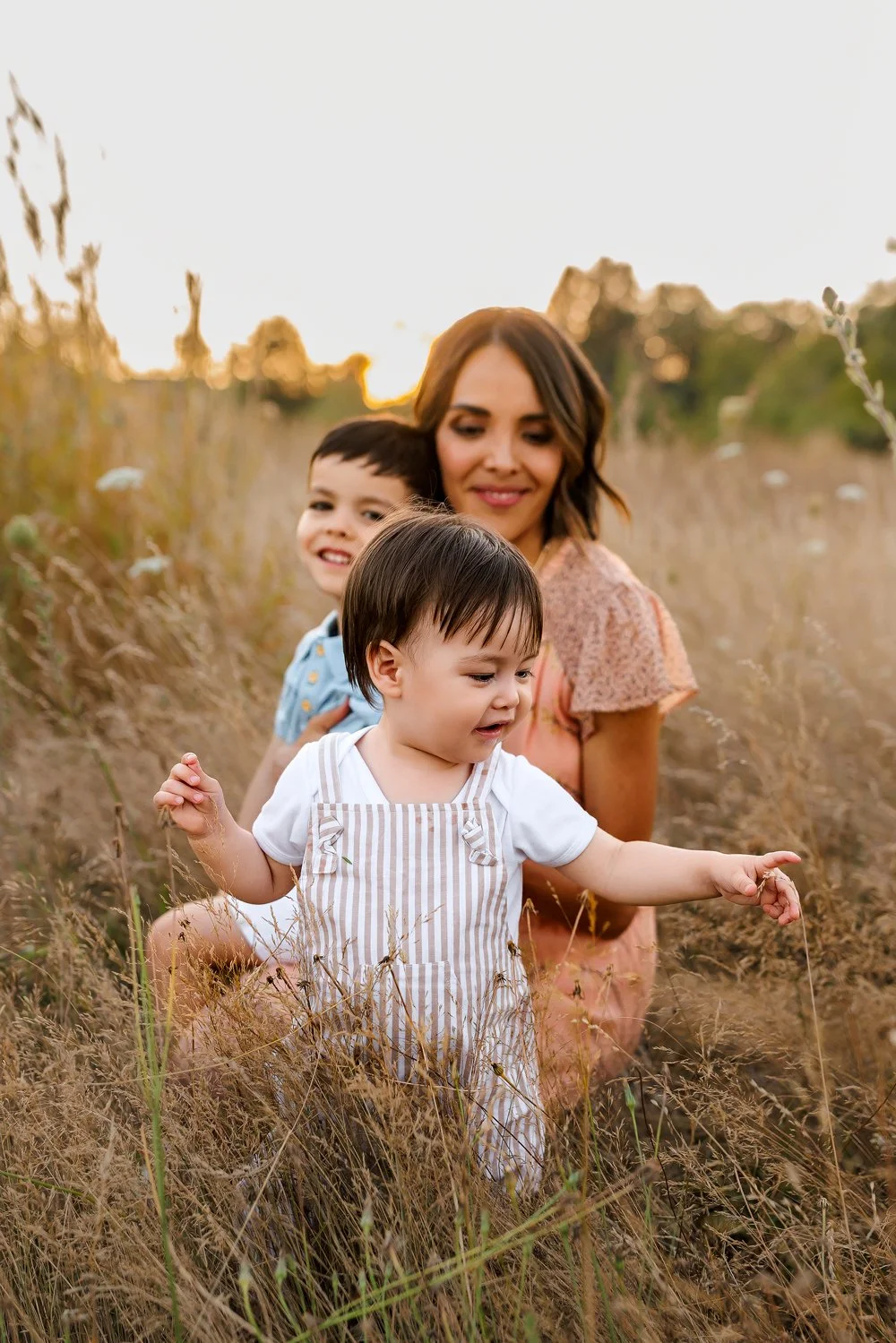 Mother sitting in a field at sunset with her two young children during a family photography session