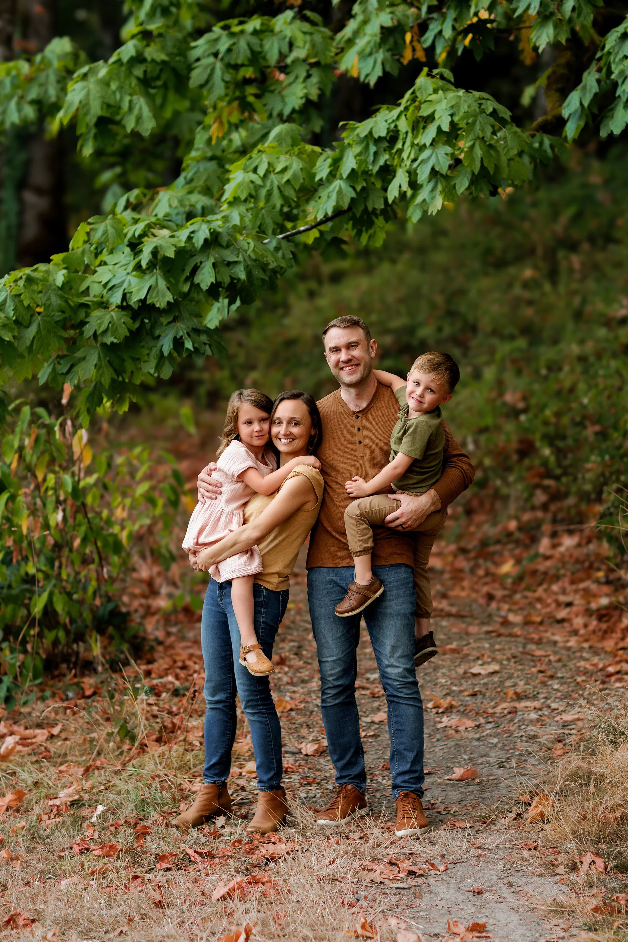 Family of four standing on wooded path in Salem Oregon with dad facing camera and arms wrapped around family