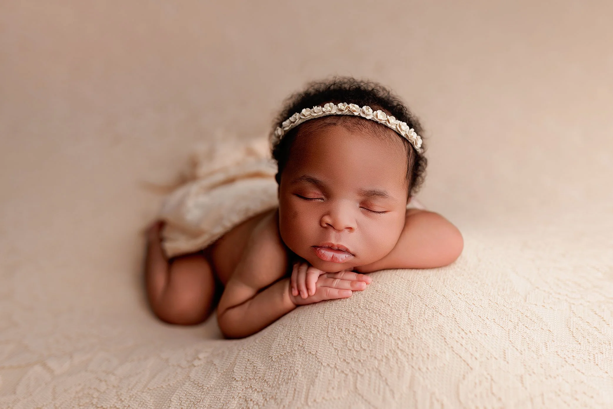 Peacefully sleeping newborn baby girl posed on soft neutral blanket wearing delicate floral headband