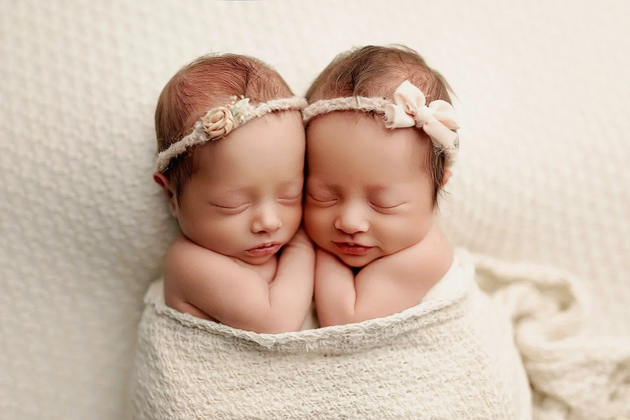 Twin newborn babies peacefully sleeping side by side with matching headbands