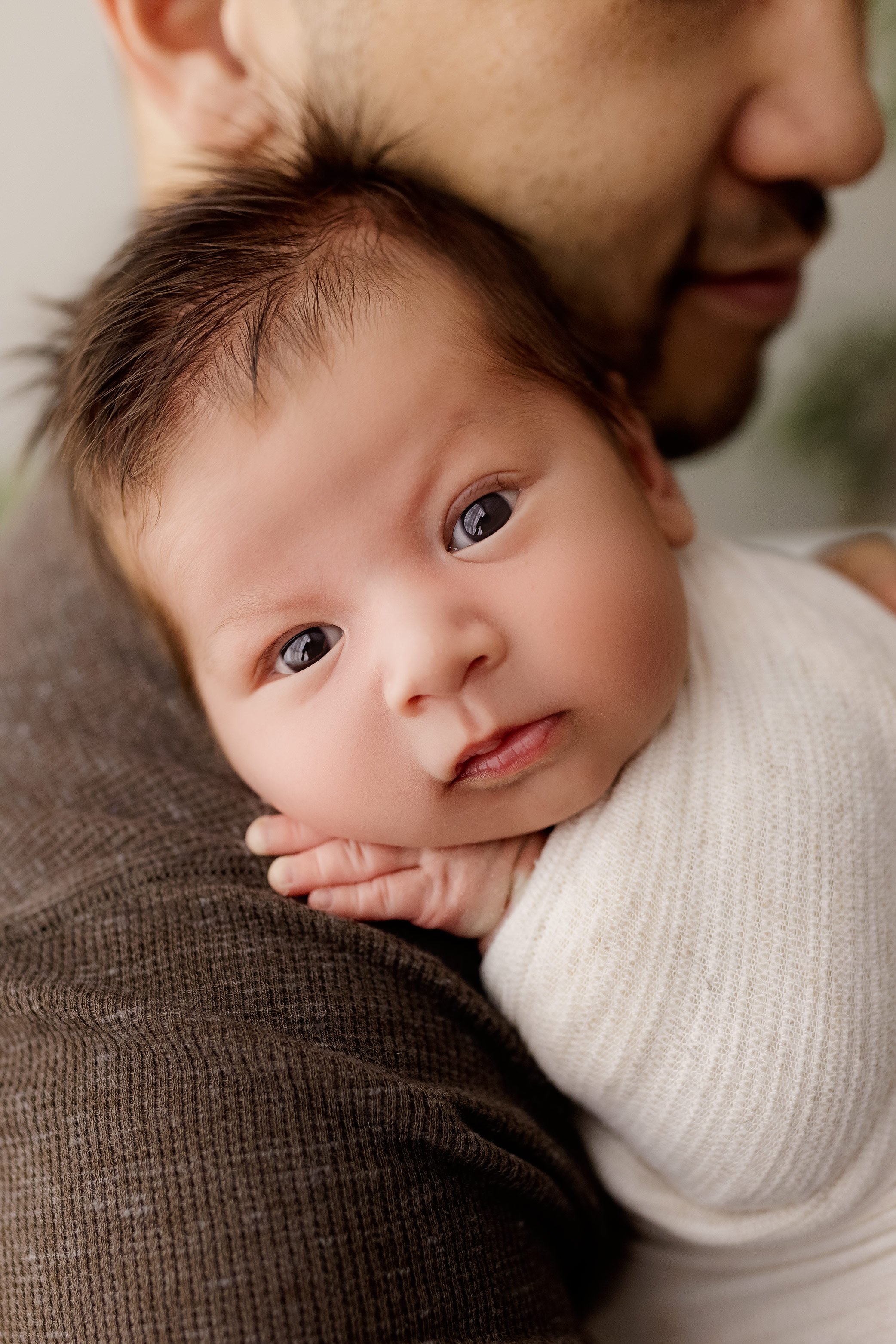 Close up portrait of newborn baby boy resting on parent shoulder in studio.