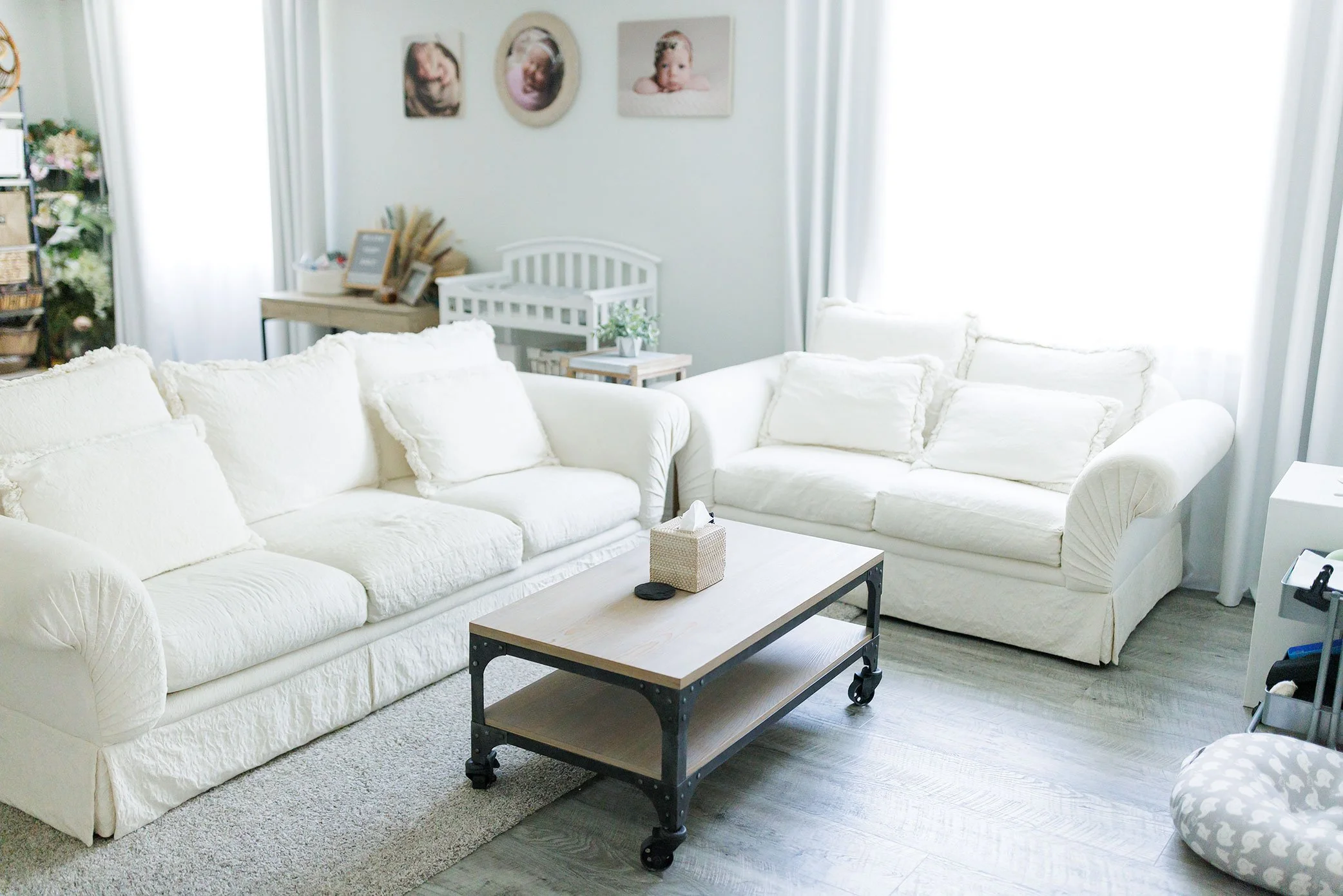 Bright, neutral newborn photography studio seating area with white couches and crib, creating a calm and welcoming space for families